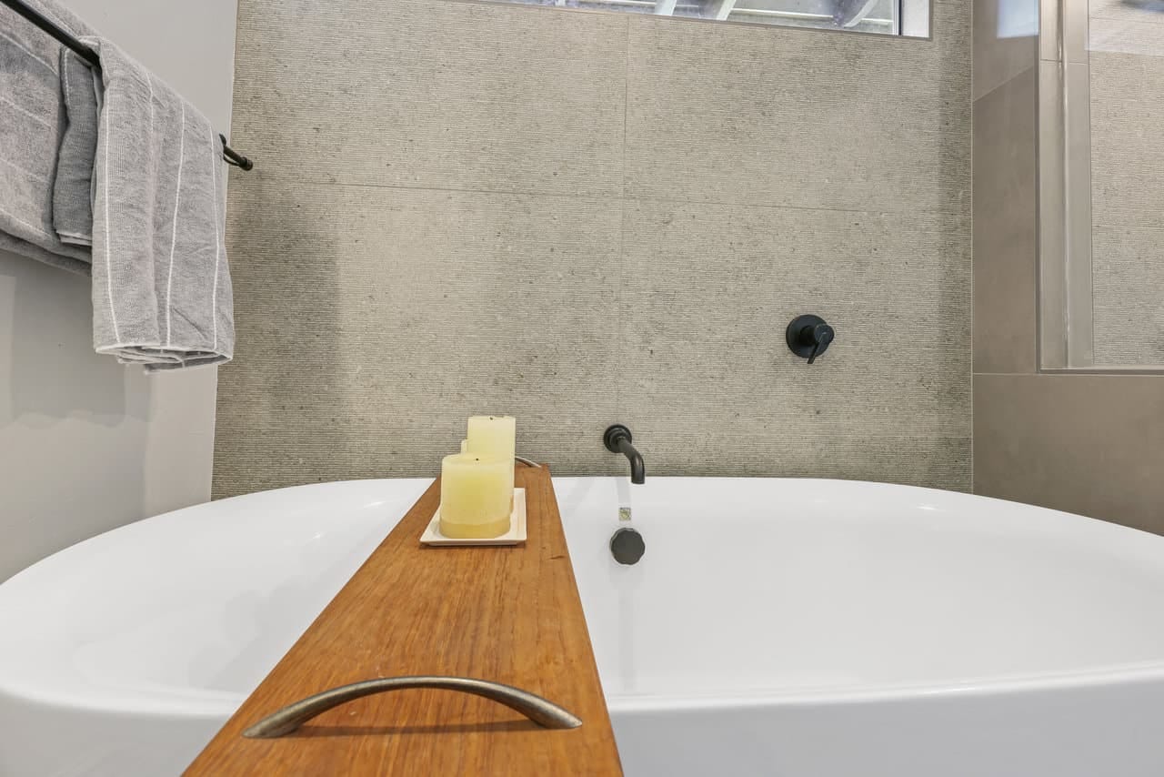 Freestanding white soaking tub with wood bath caddy and concrete-look tile wall