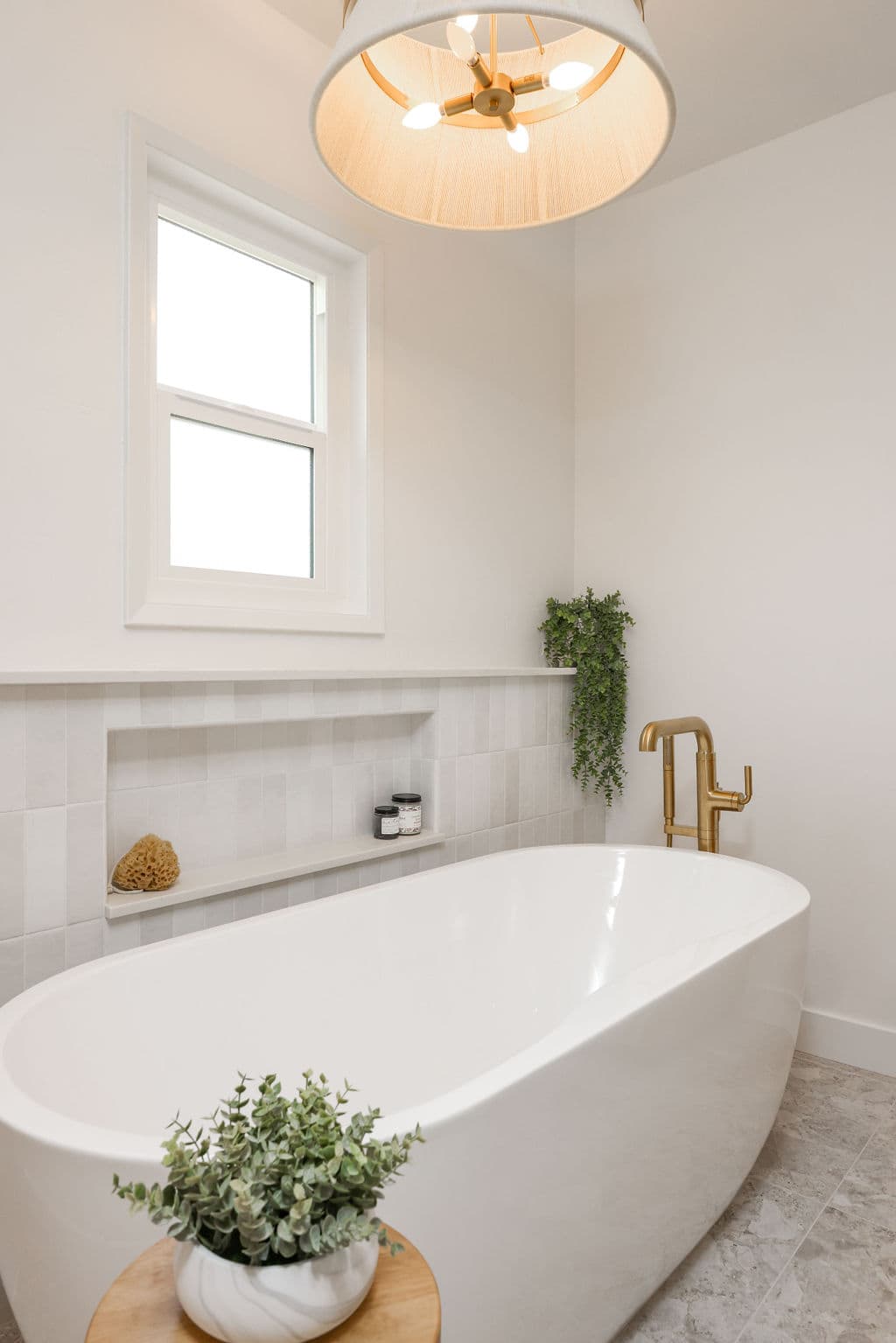 Freestanding white tub under window with brass filler and trailing greenery