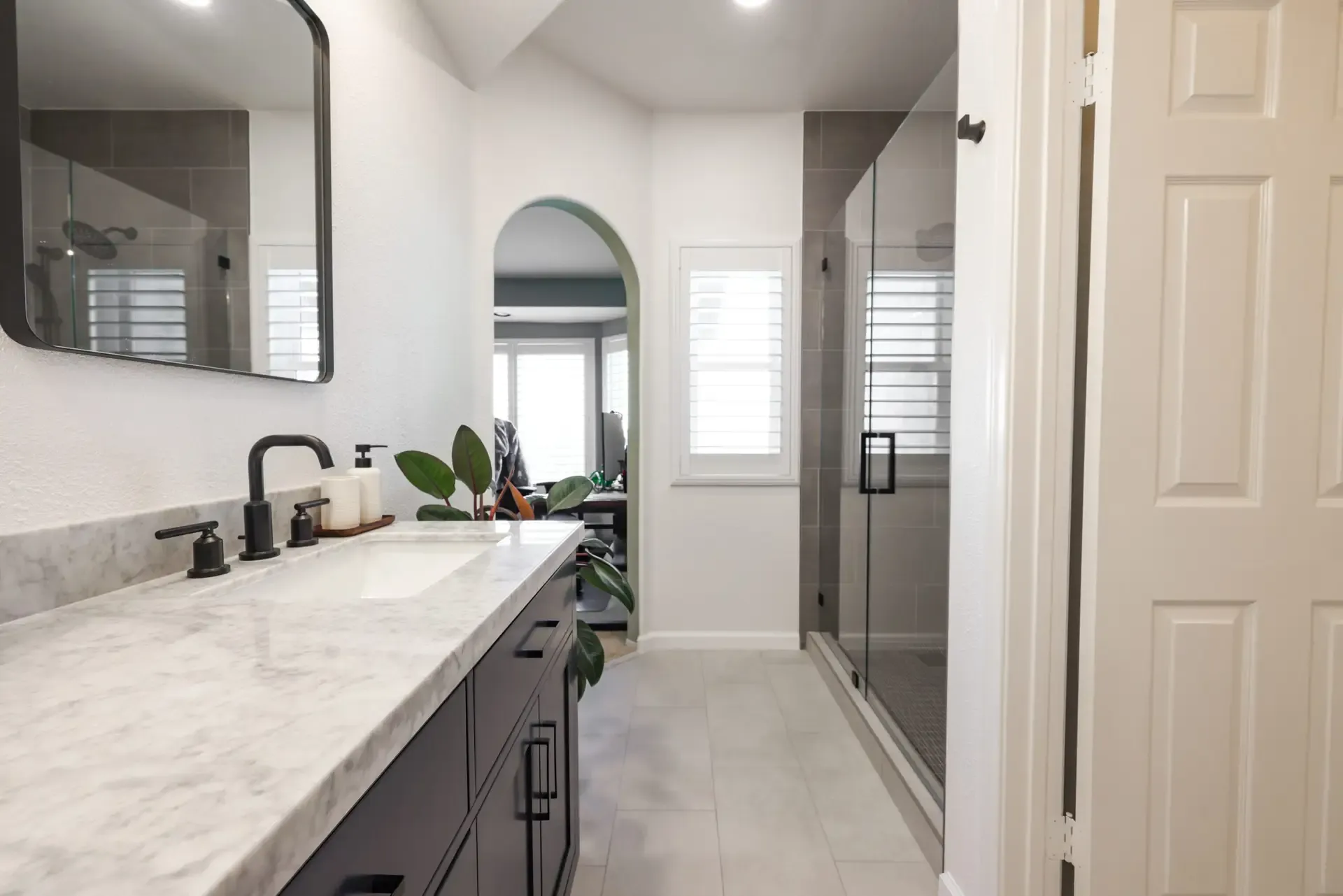 Galley bathroom with dark vanity, marble top, and glass corner shower