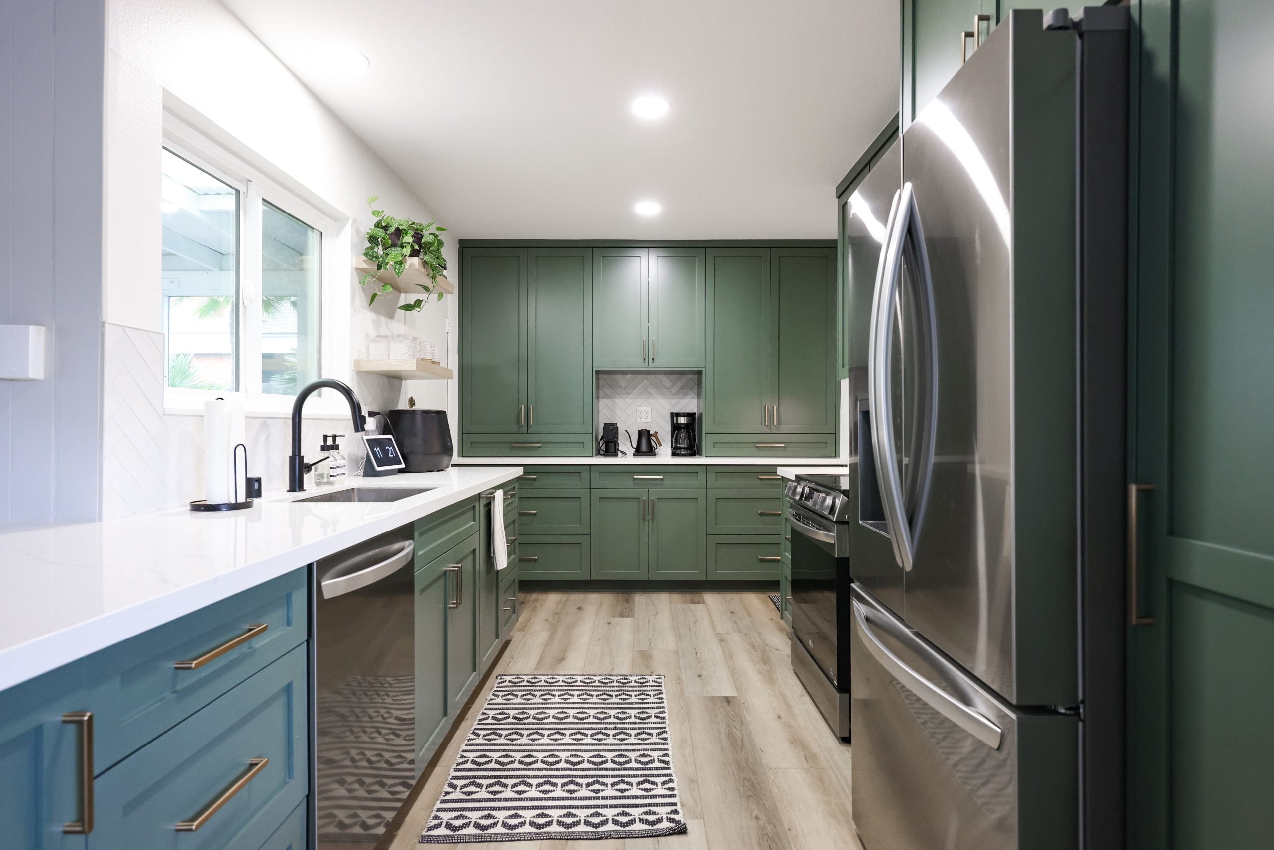 Galley kitchen featuring sage green cabinets, light wood flooring and stainless steel refrigerator
