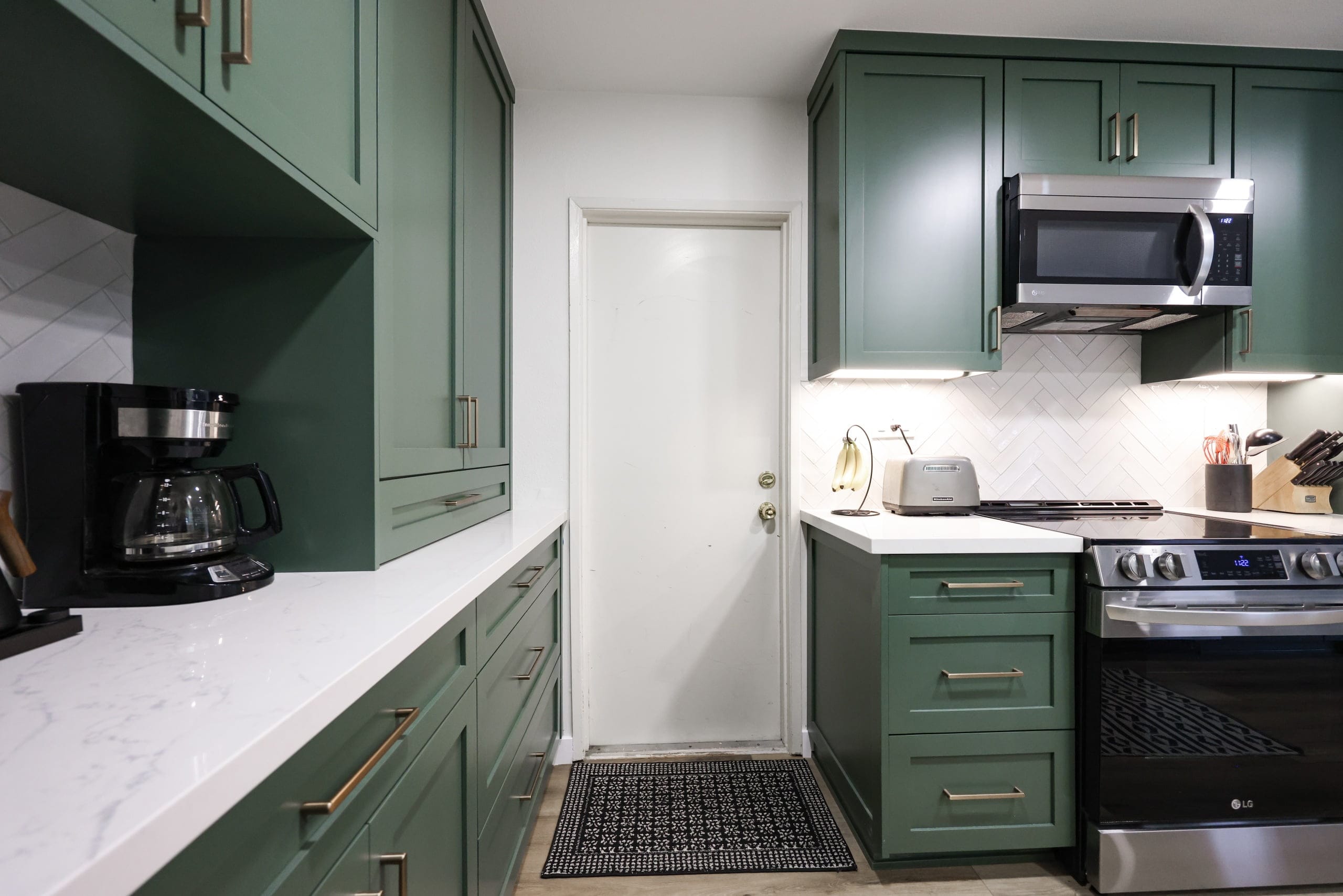 Galley kitchen in deep green cabinets with white quartz counters and herringbone backsplash