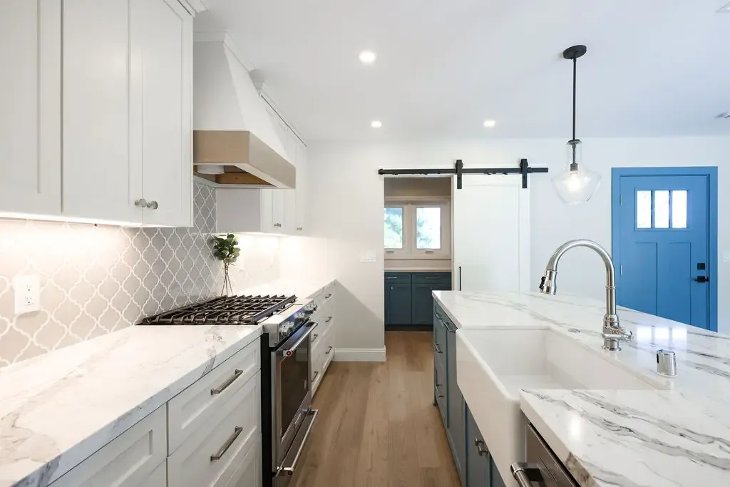 Galley kitchen with white marble waterfall island, arabesque tile backsplash, and blue front door