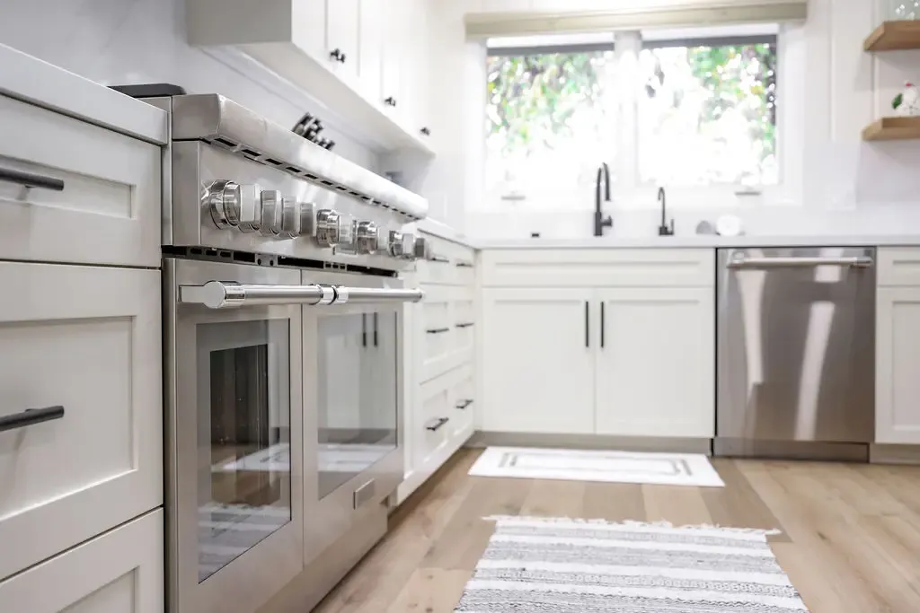 Galley kitchen with white shaker cabinets, stainless appliances and oak floors