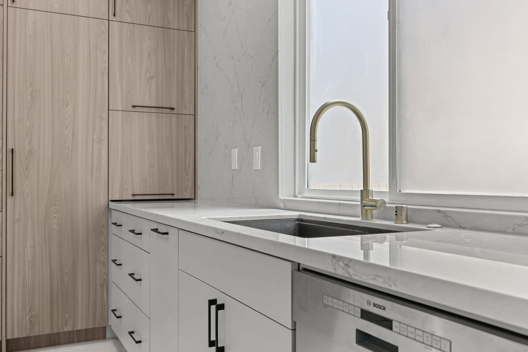 Modern kitchen with light wood cabinets, quartz counter and brass gooseneck faucet