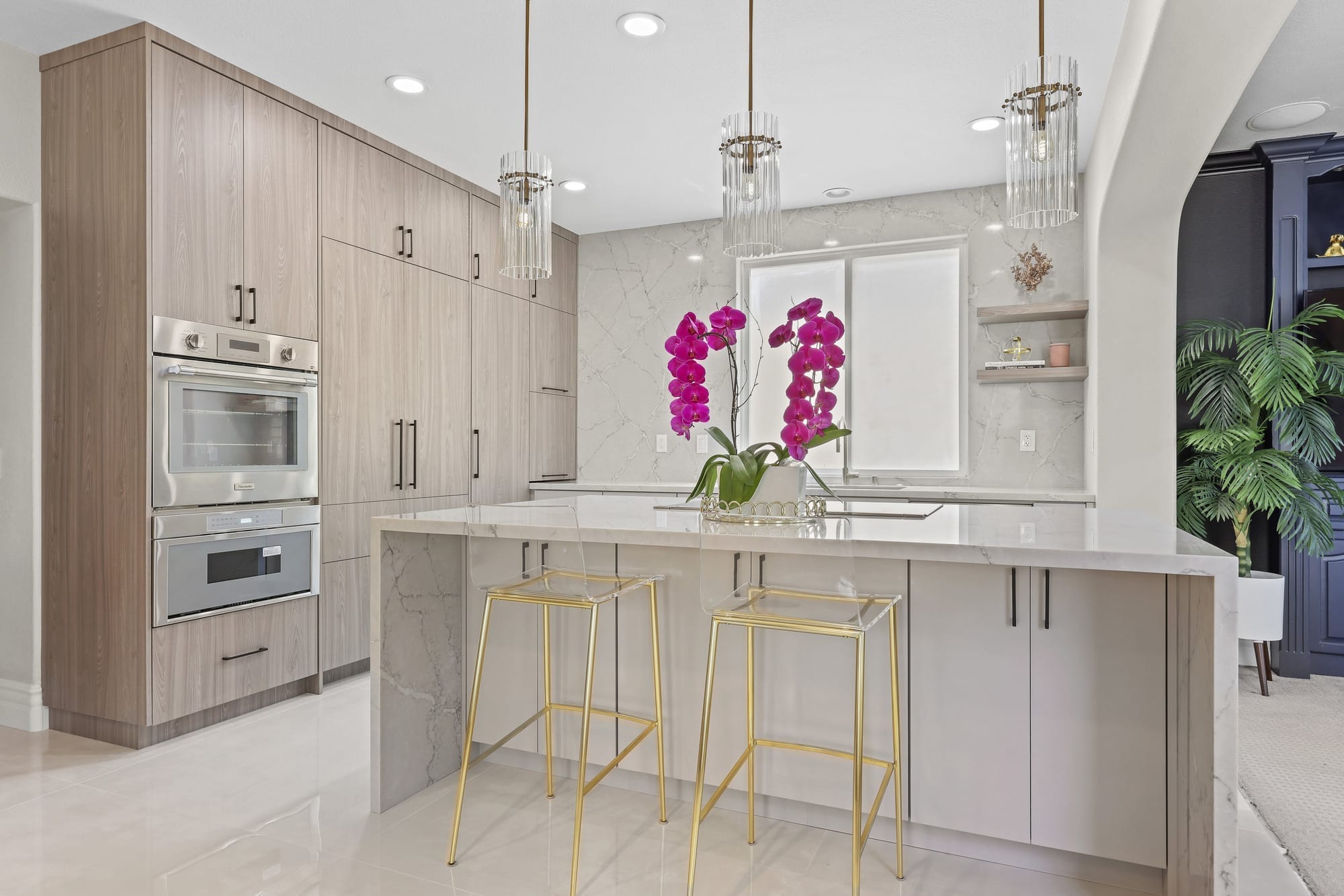 Open kitchen with waterfall quartz island, gold bar stools and wood cabinetry
