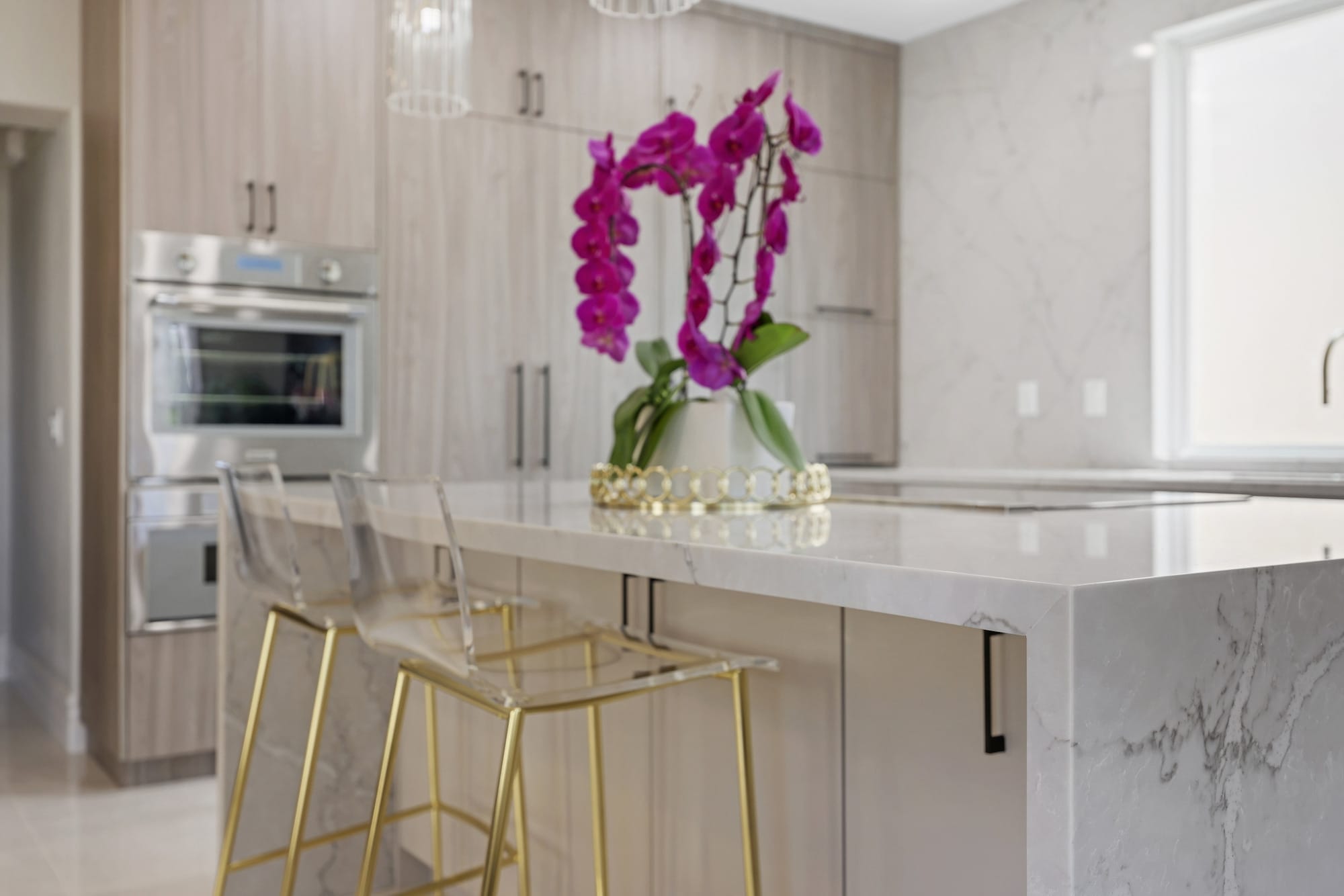 Quartz waterfall island with acrylic gold counter stools and wood cabinet kitchen