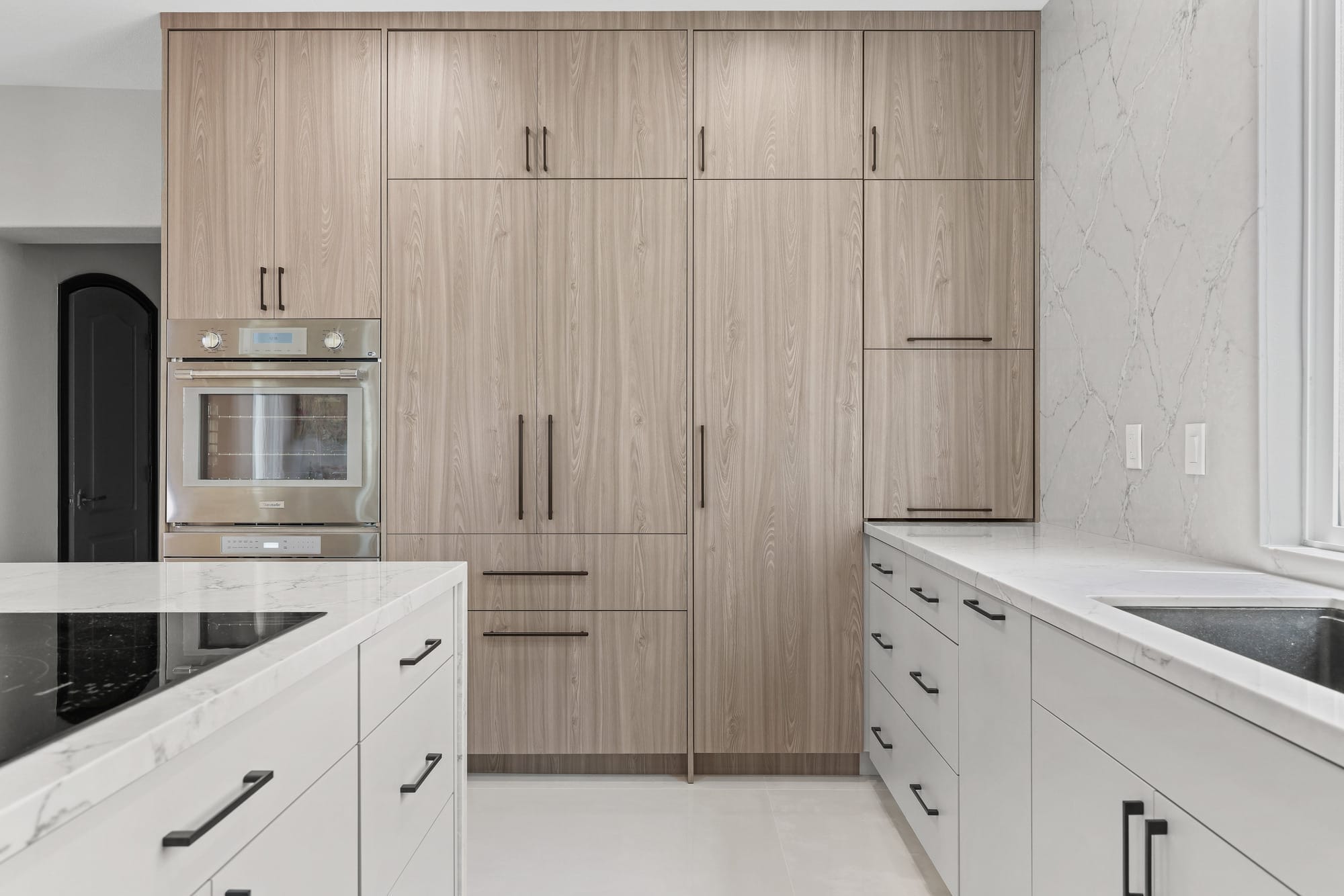 Wood-paneled kitchen with built-in wall oven and marble waterfall island counters