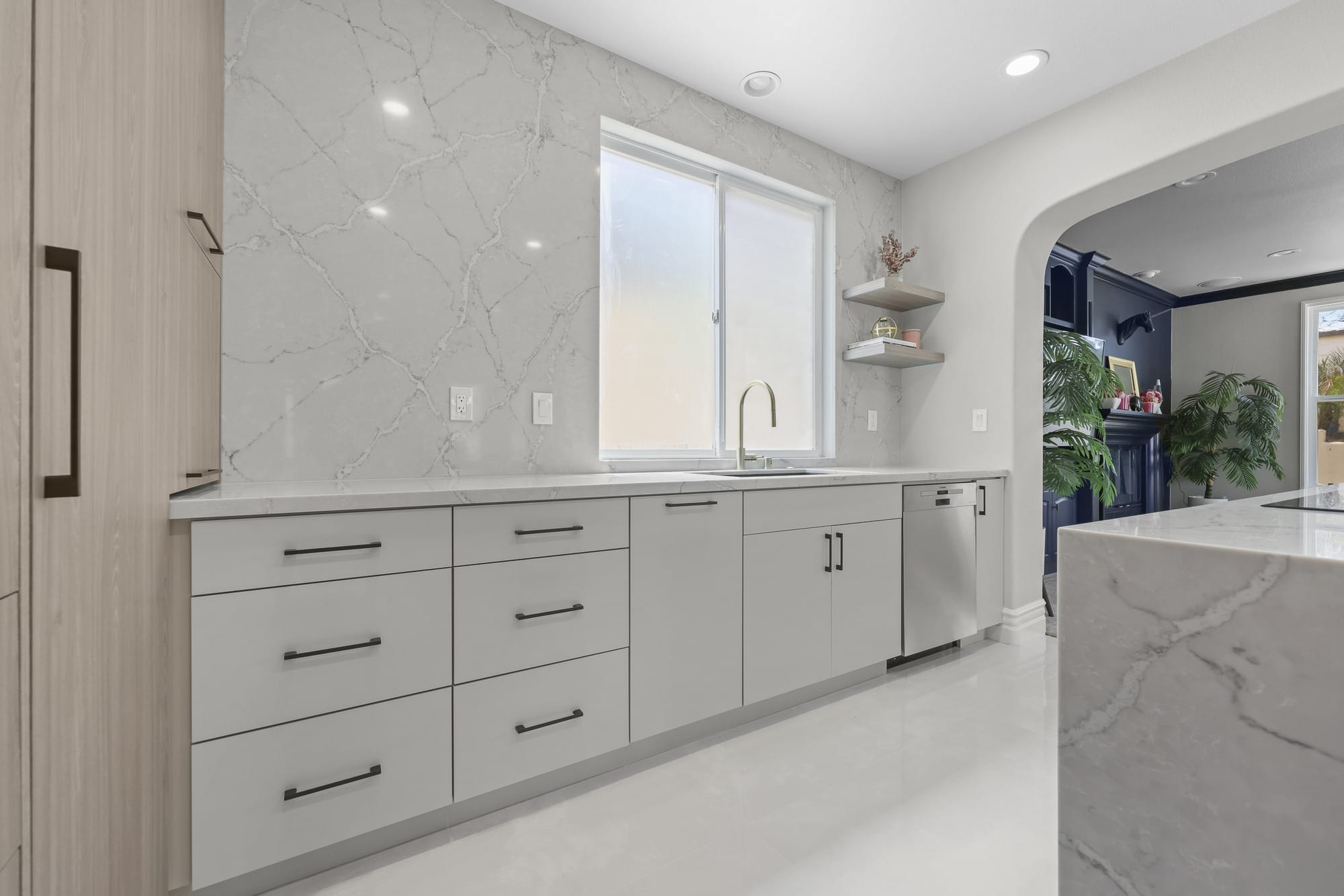 Kitchen run with marble slab backsplash, white shaker cabinets and brushed gold faucet