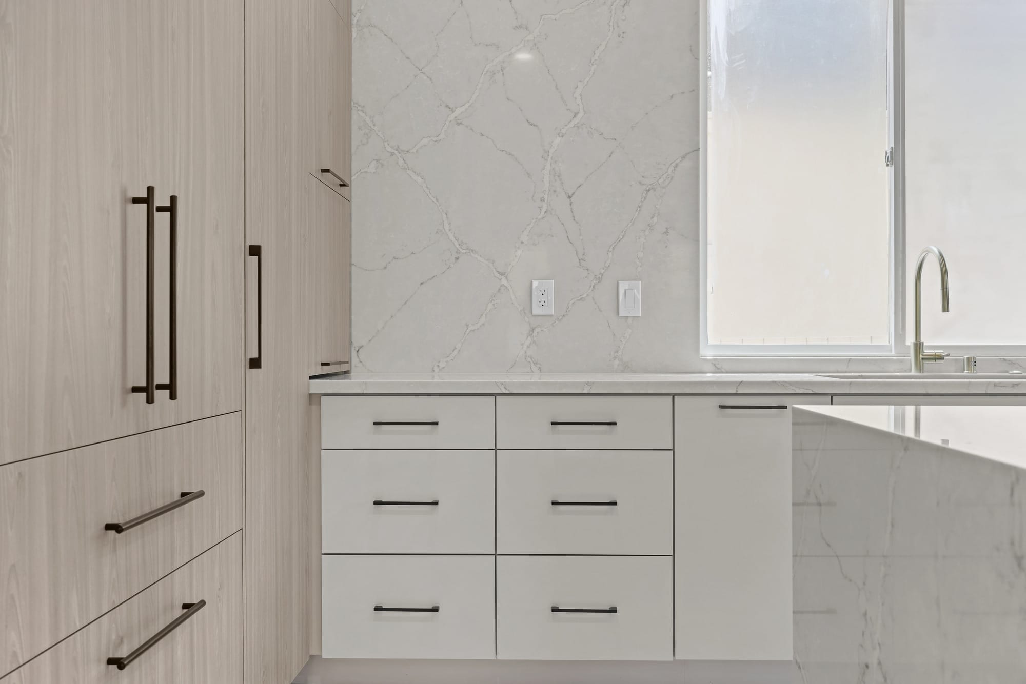 Light oak tall cabinets beside white drawers and veined quartz waterfall countertop