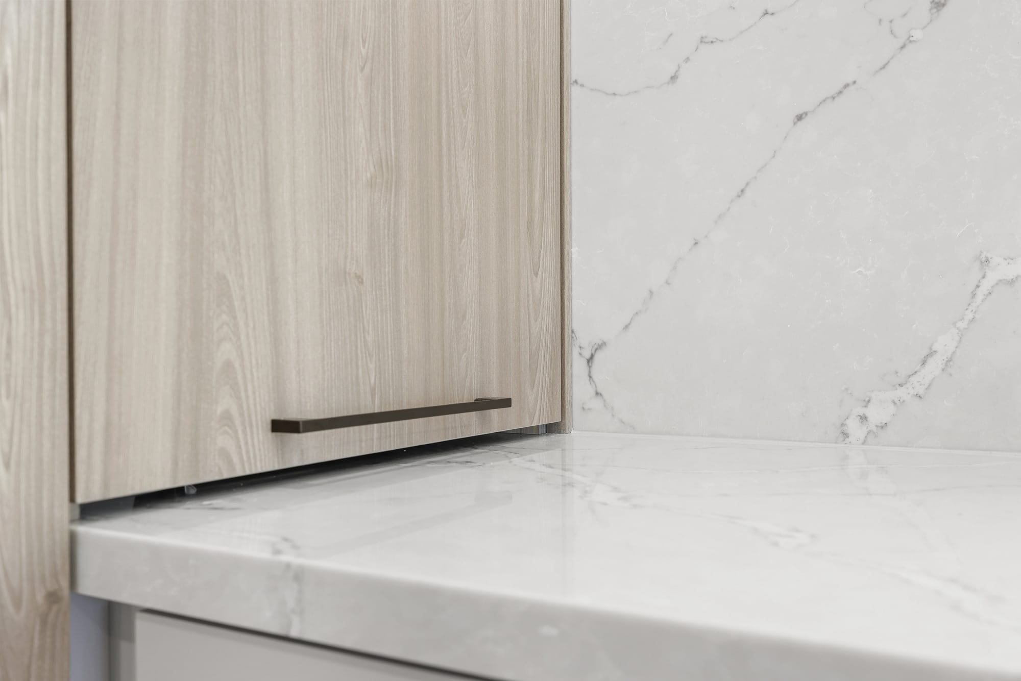 Close-up of oak cabinet panel meeting a white marble-look waterfall countertop edge