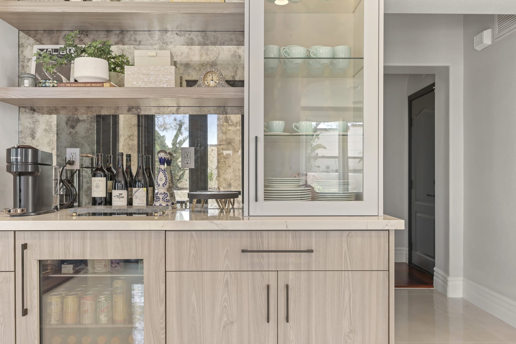 Coffee and wine bar with mirrored backsplash, floating shelves and glass-front cabinet