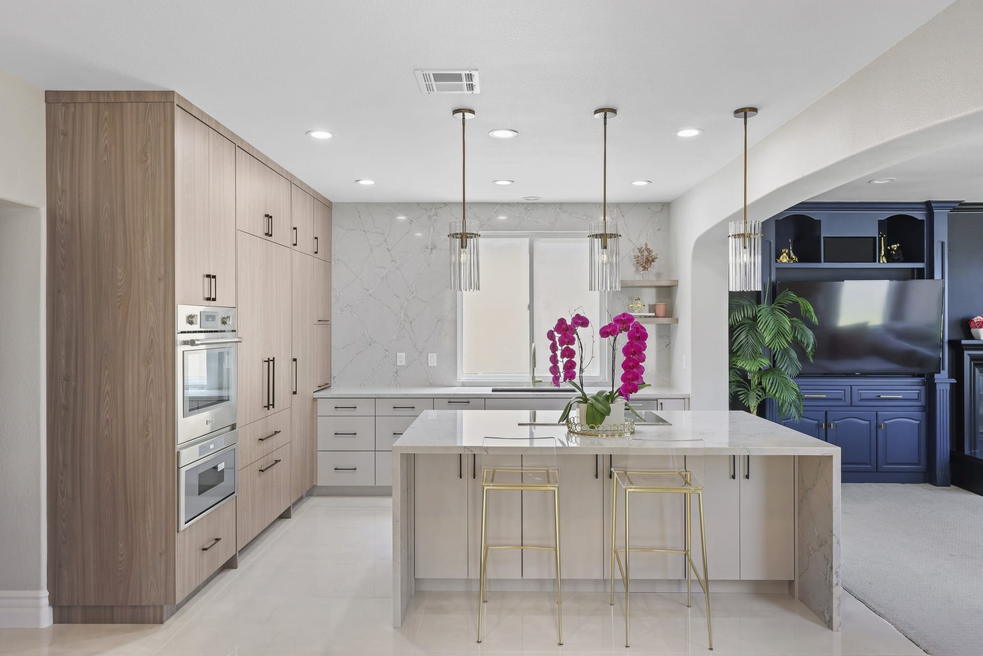 Bright kitchen with marble island, oak and gray cabinets and slim brass pendants