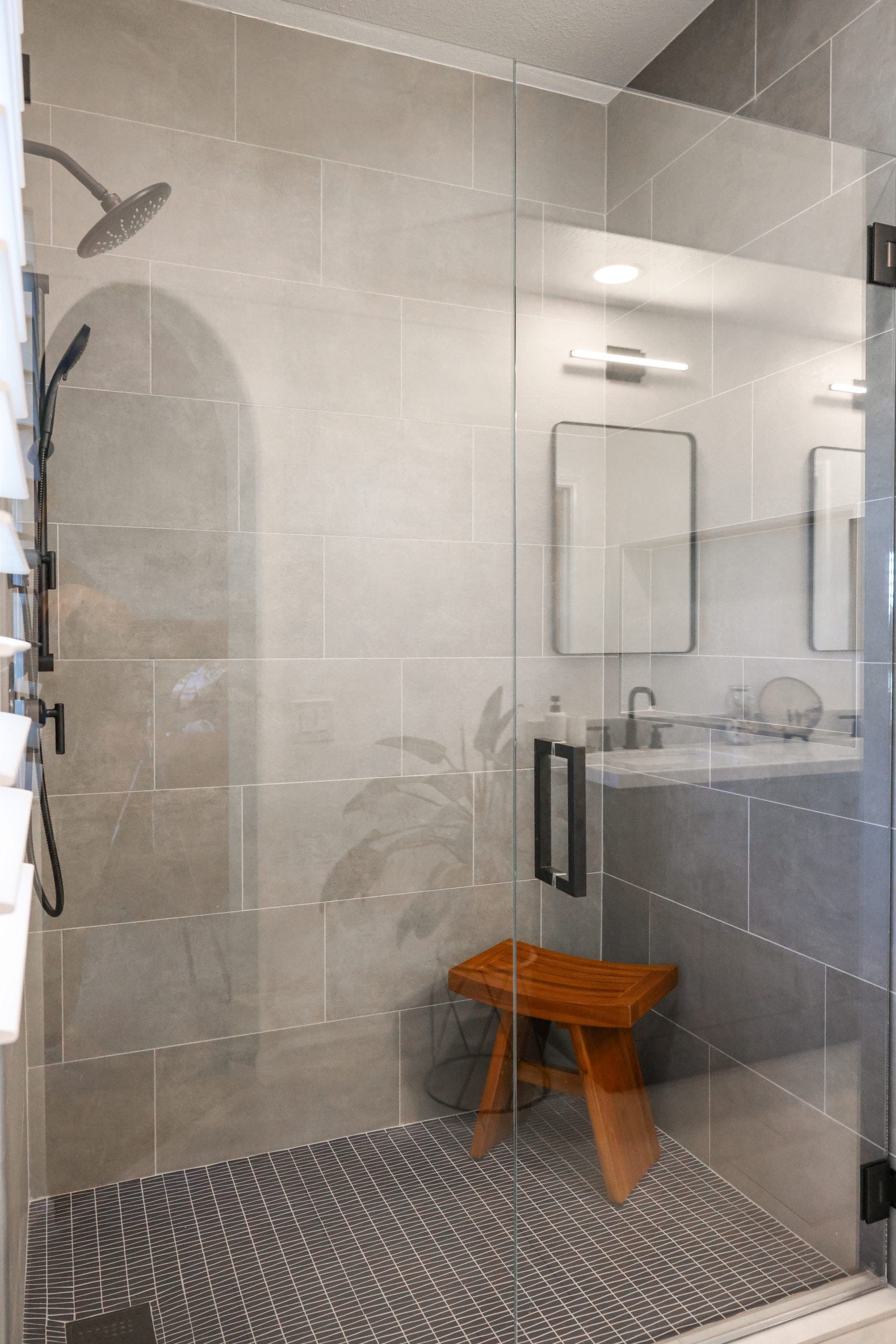 Glass-enclosed shower with light gray tile, teak stool and tiled floor