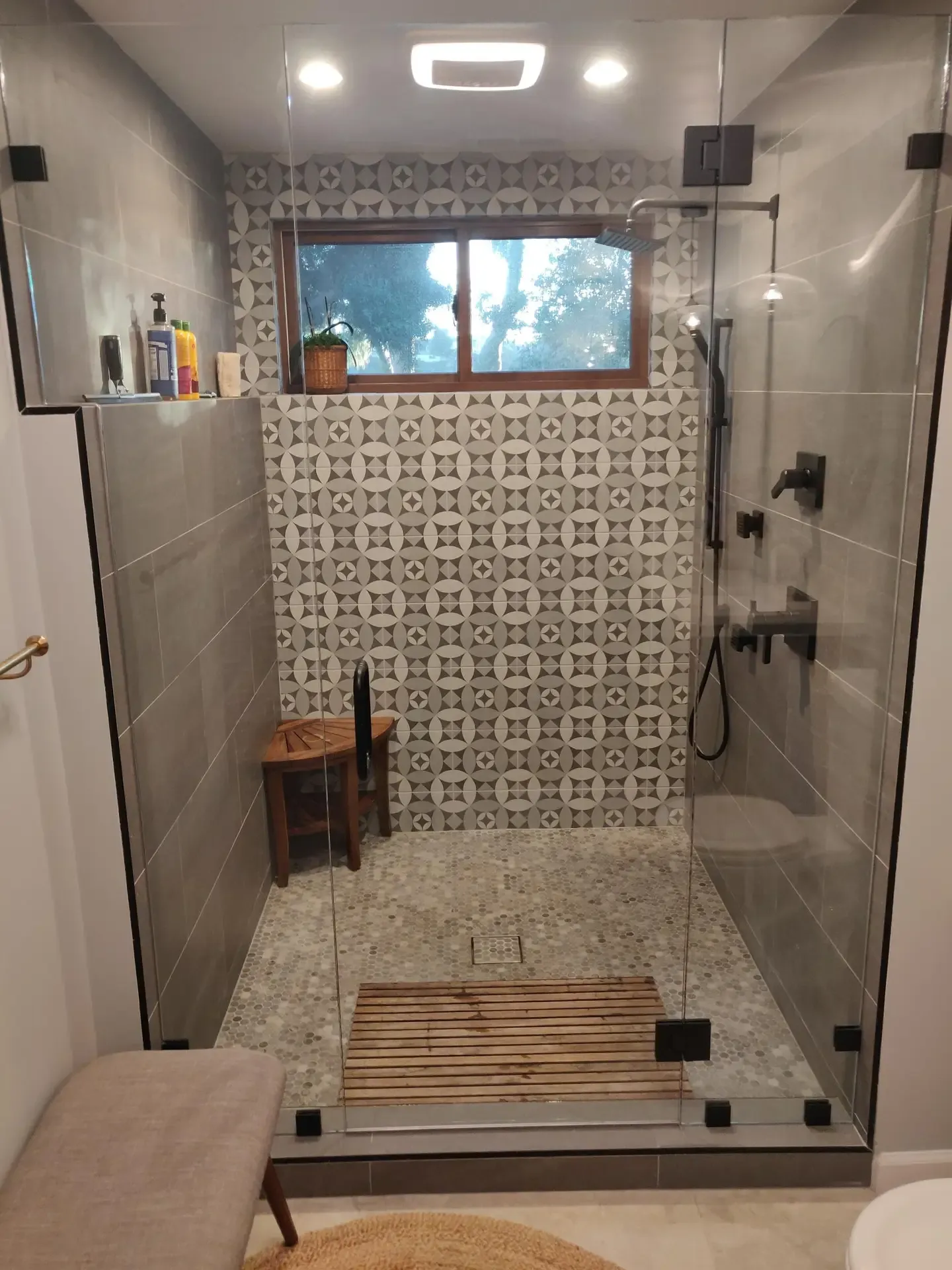 Glass-enclosed walk-in shower with patterned accent tile and teak floor bench