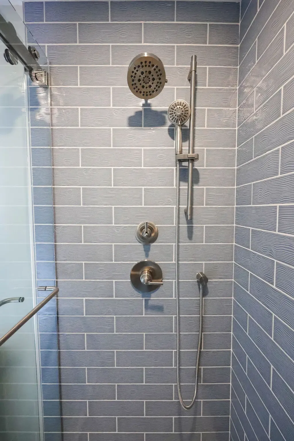 Glass shower enclosure with blue subway tile and brushed nickel fittings