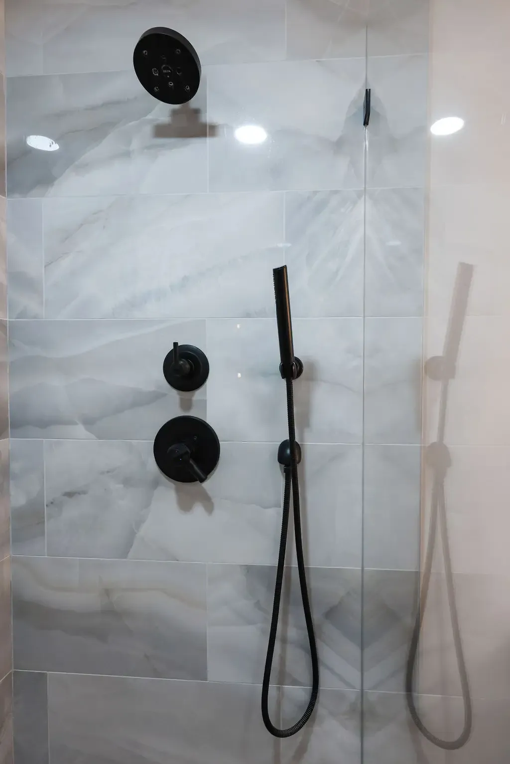Glass shower interior with matte black fixtures and veined marble wall tile