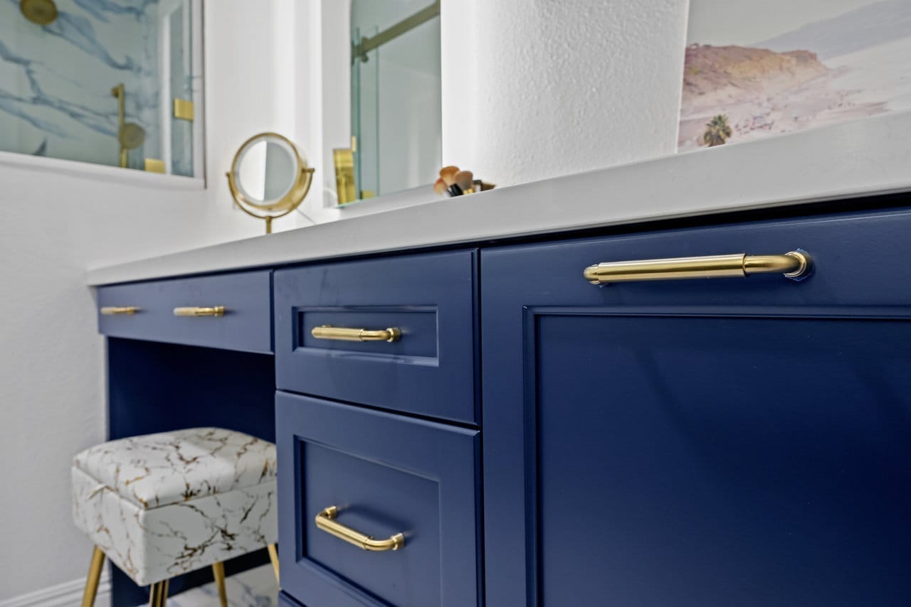 glossy navy vanity drawers and door with brass hardware beside marble-pattern accent stool