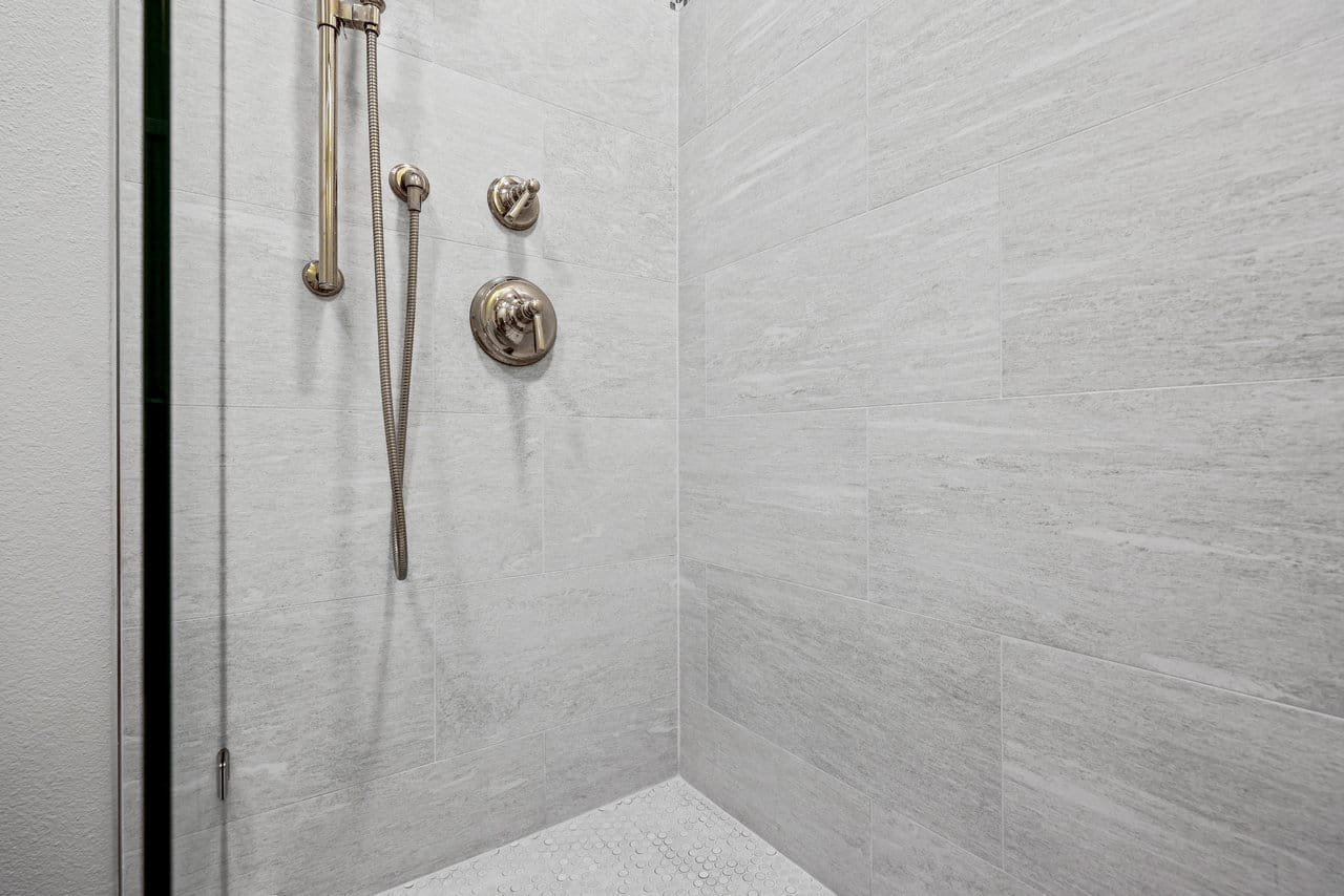 Gray porcelain tile shower with handheld sprayer and pebble mosaic floor