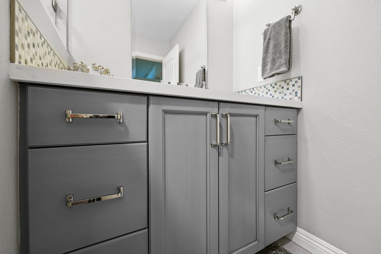 Gray shaker bathroom vanity with polished nickel pulls and mosaic tile accent