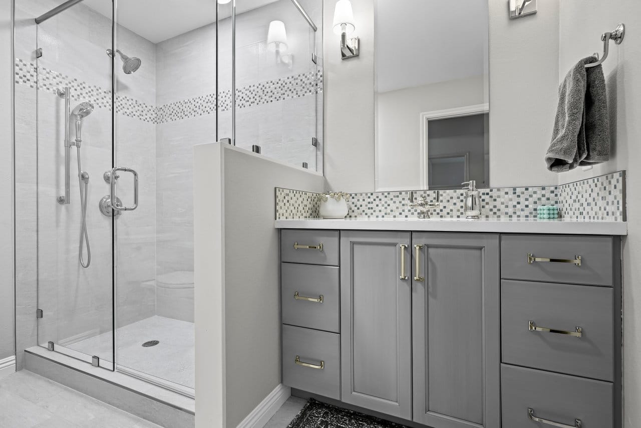 Gray shaker vanity and frameless glass shower with mosaic accent stripe and quartz counter
