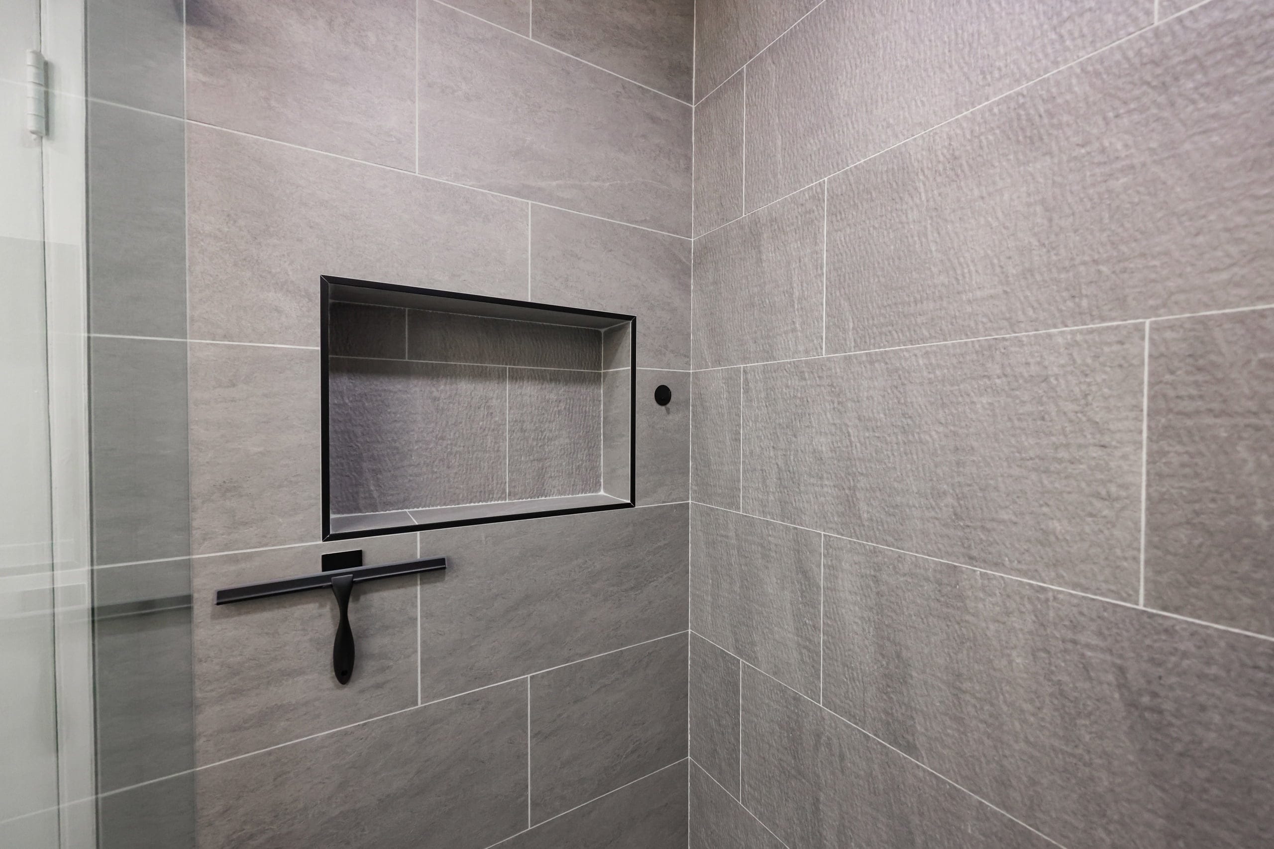 gray stone-look shower tile with recessed niche and black squeegee