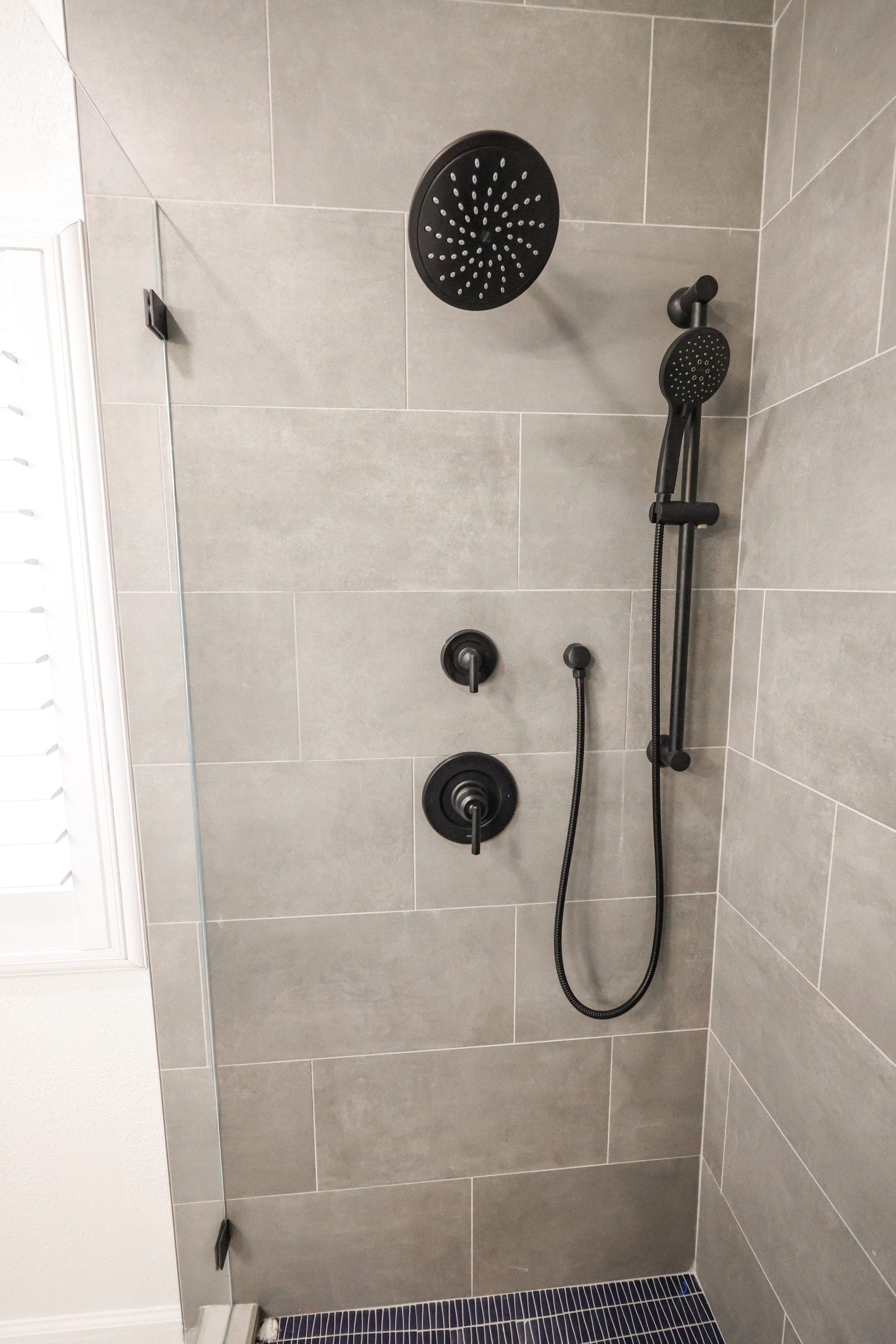 Gray tile shower with matte black rainfall head and handheld sliding bar