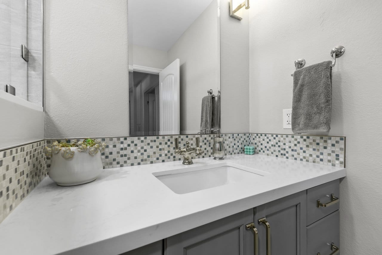 Gray vanity bathroom with quartz top, mosaic tile backsplash and large frameless mirror