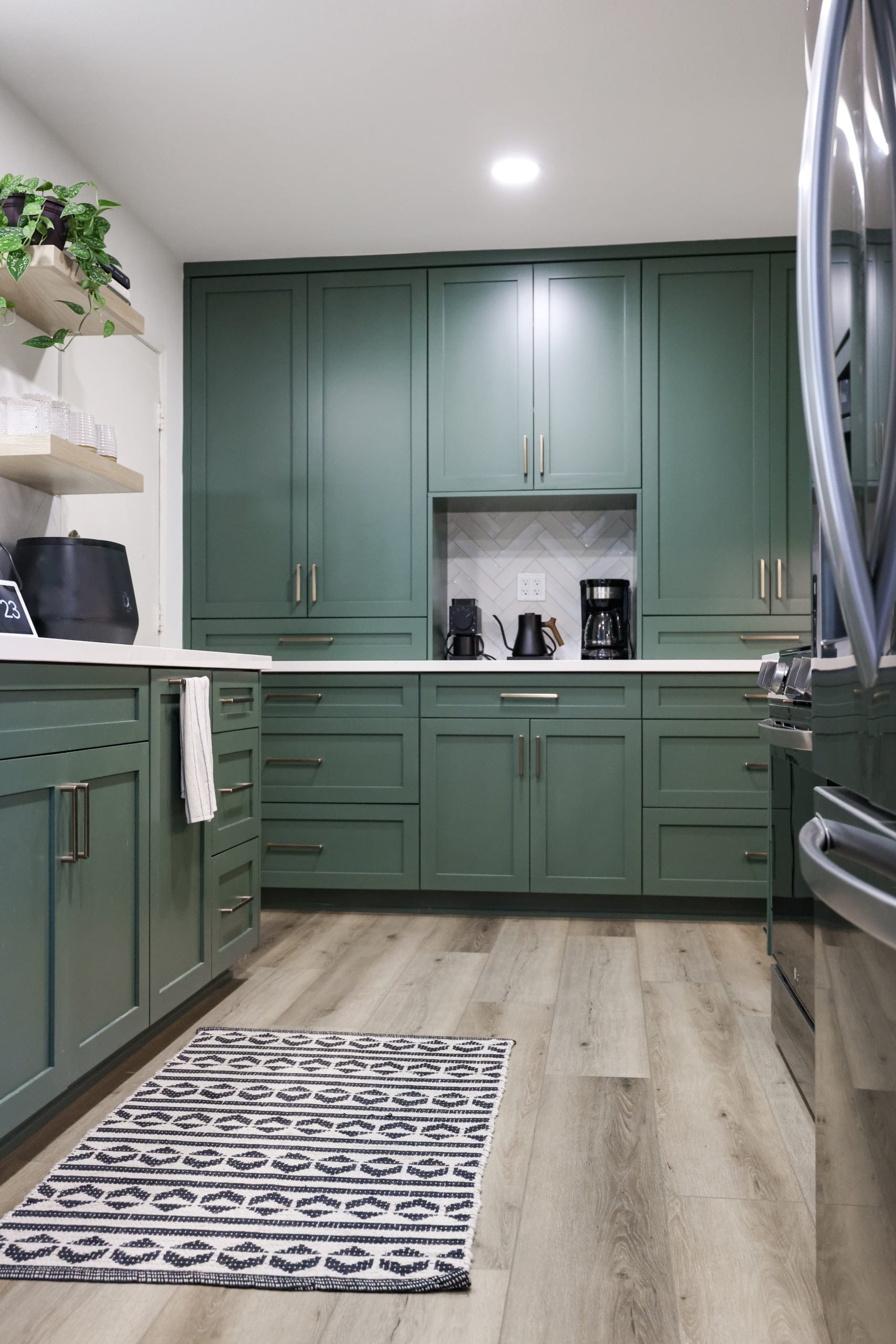 Green flat-panel kitchen cabinetry with stainless steel fridge and patterned runner rug