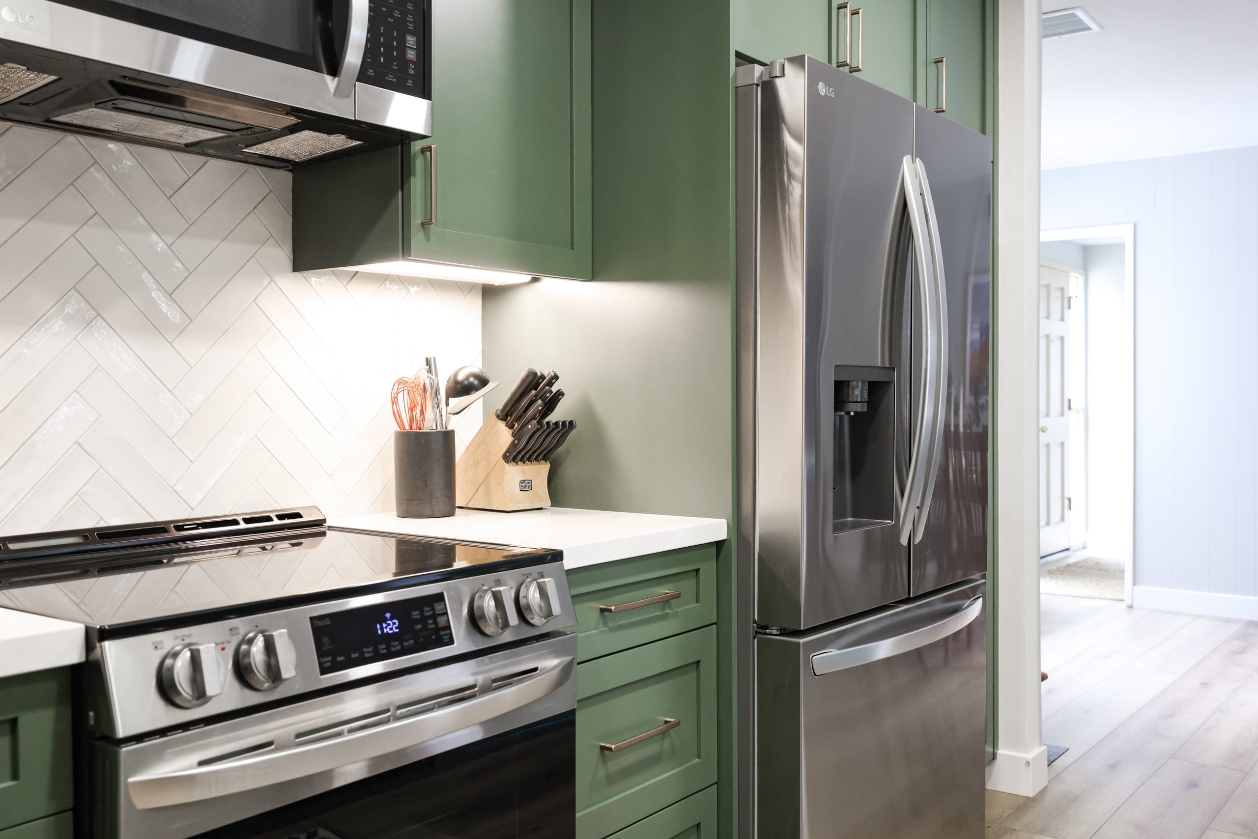 Green kitchen with stainless French-door refrigerator, gas range and marble-look backsplash
