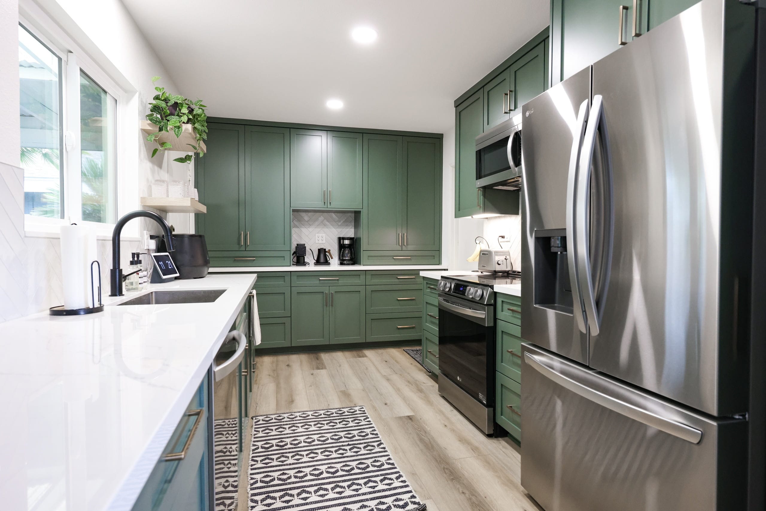 Green shaker kitchen with white quartz counters, stainless appliances and patterned tile floor
