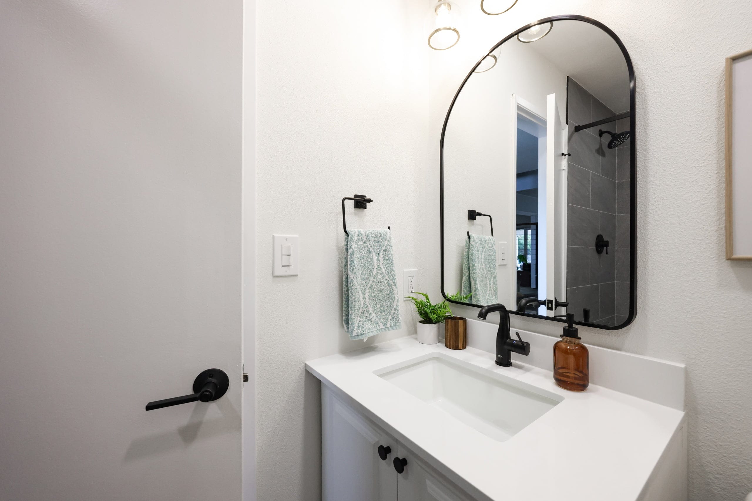 guest bath vanity with white quartz top, arched mirror and black fixtures