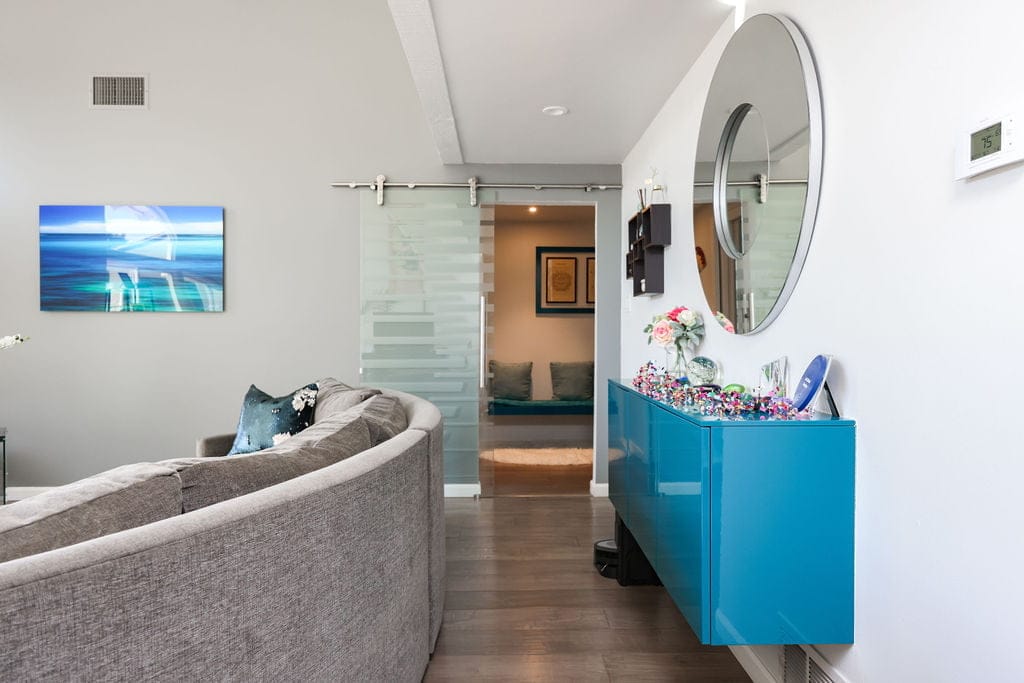 Hallway with frosted glass barn door, glossy blue console and round mirror near curved sofa