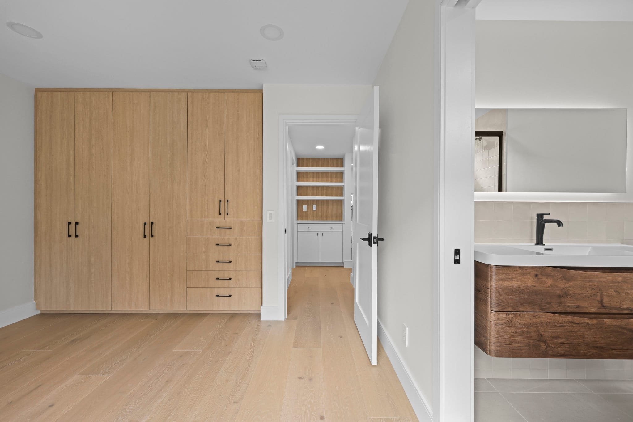 Primary bedroom with light oak wardrobe, walk-in closet and floating wood-grain vanity