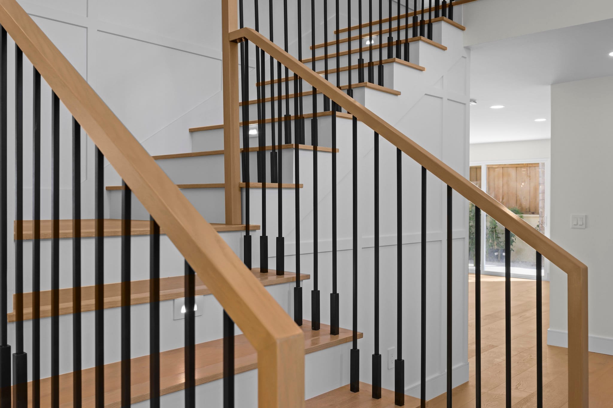 Staircase with oak treads, white shaker wainscot panels and black metal balusters
