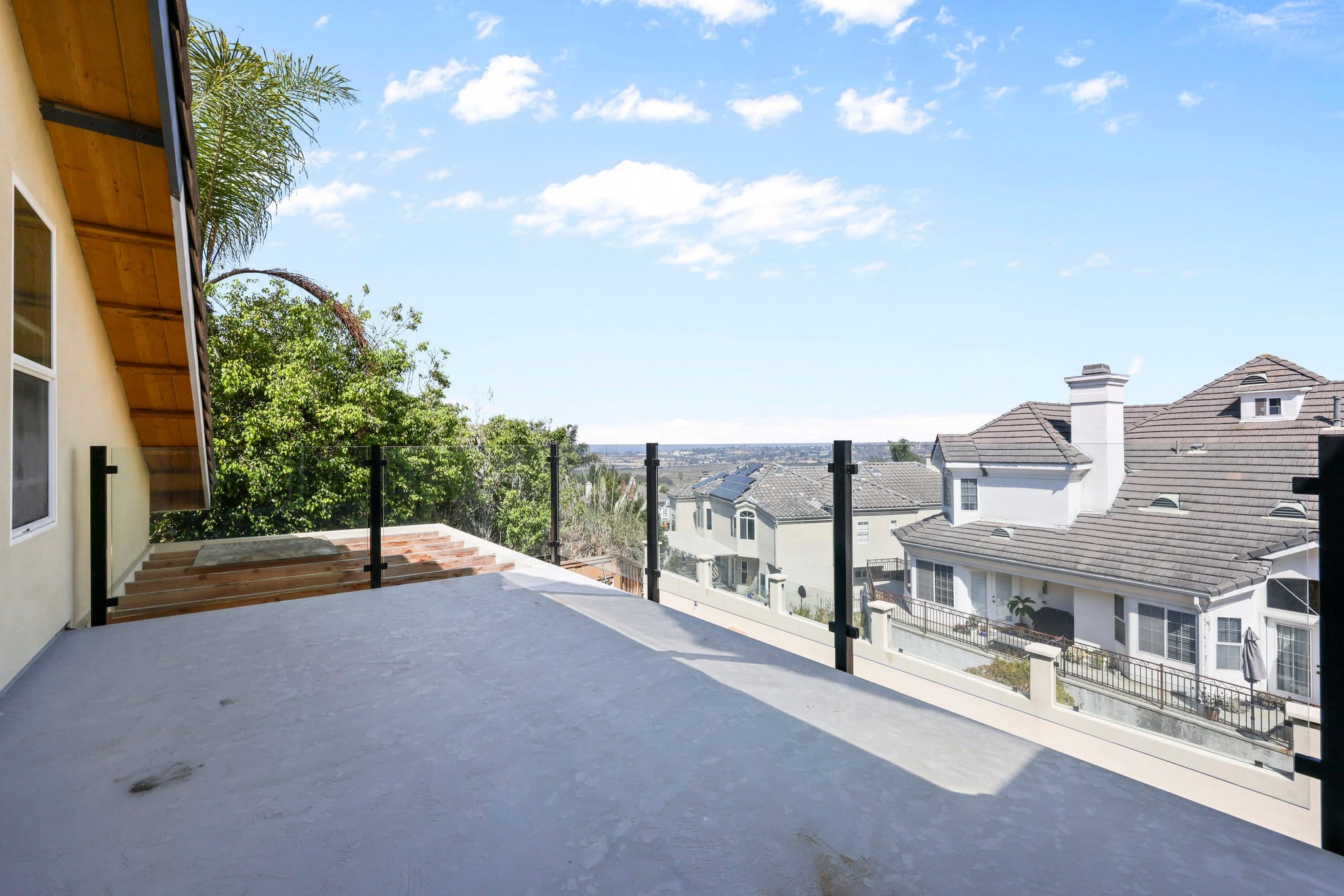 Concrete rooftop deck with glass-panel railing overlooking tile-roof neighborhood and hills