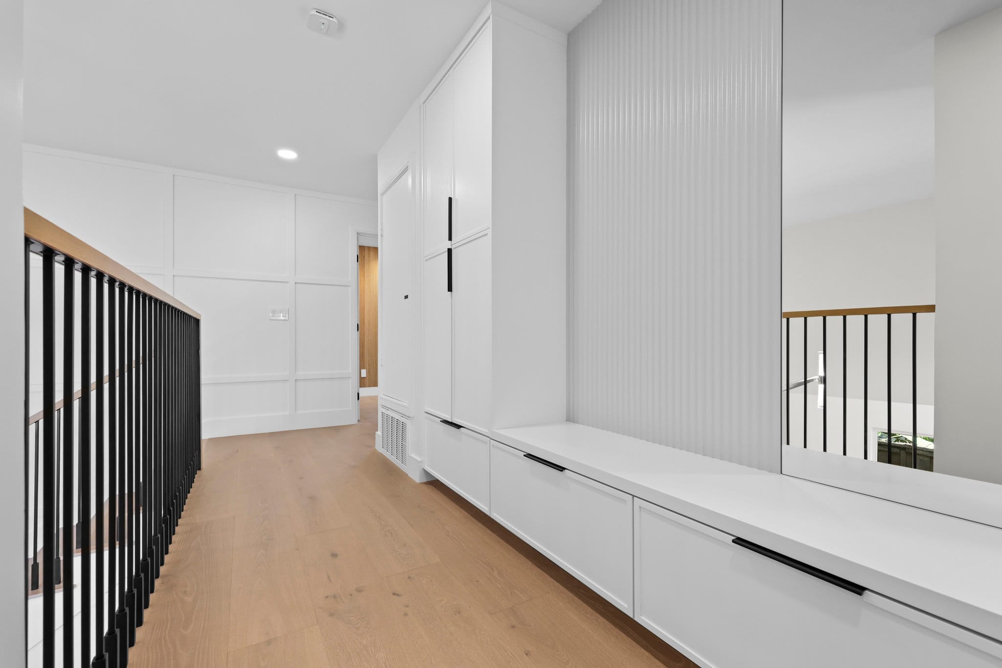 Upstairs hall with white built-in bench, fluted accent panel and black stair railing