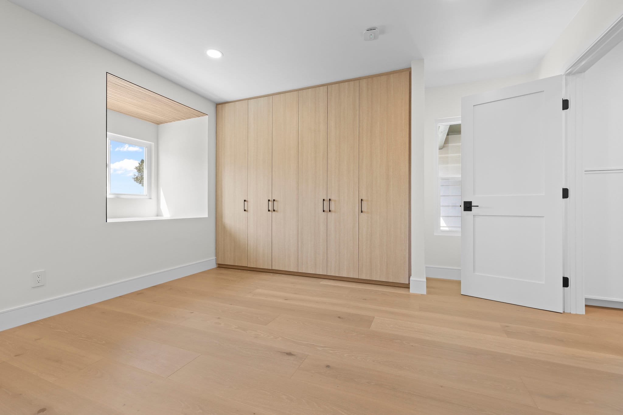 Modern bedroom with light oak floor-to-ceiling wardrobe and pale wood flooring