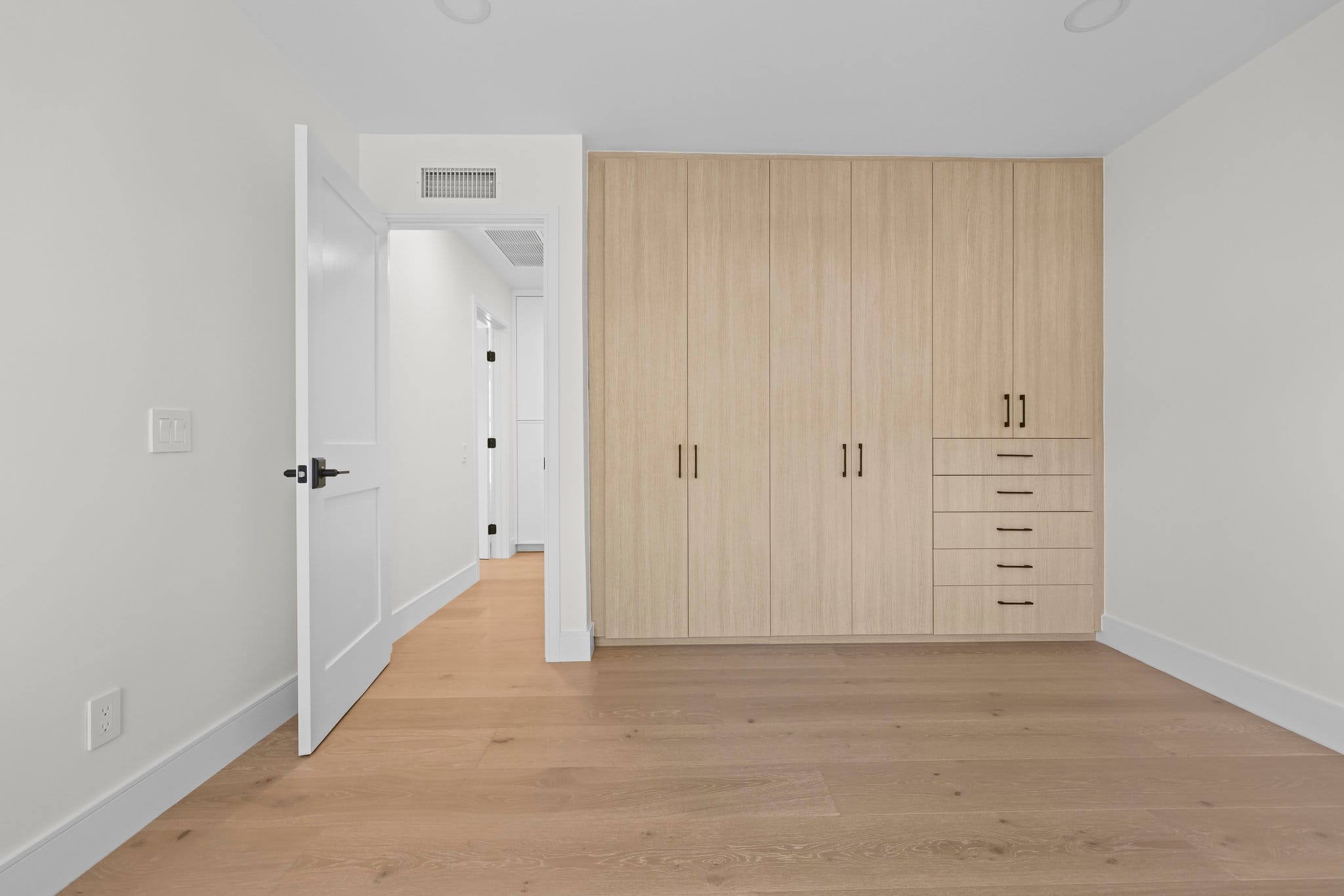 Empty bedroom with light oak built-in wardrobe, drawers and white shaker door