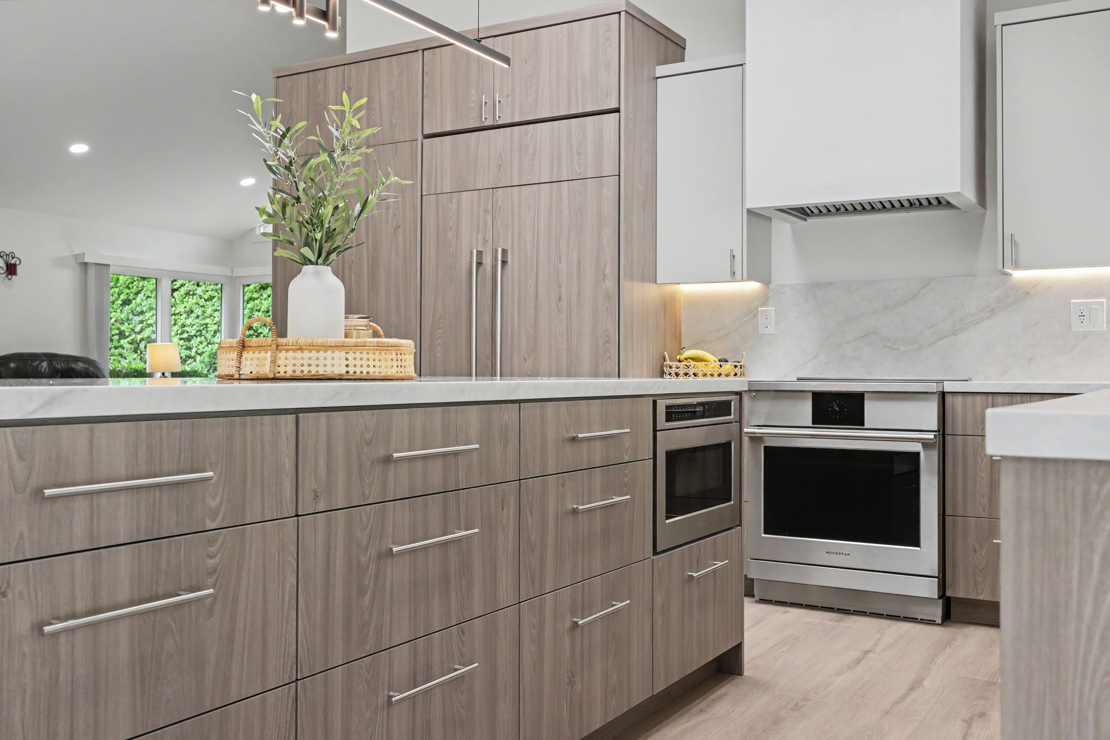 Detailed view of wood-grain kitchen island drawers, a built-in microwave, and a stainless steel range against a white marble backsplash.