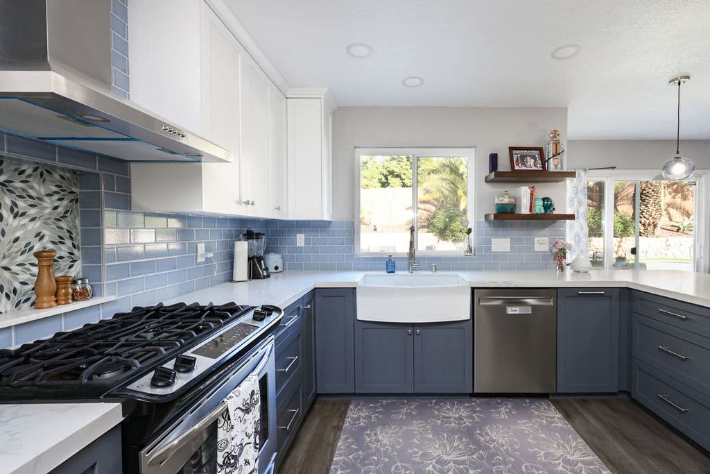 Kitchen with gas cooktop, farmhouse sink and blue subway tile under bright window