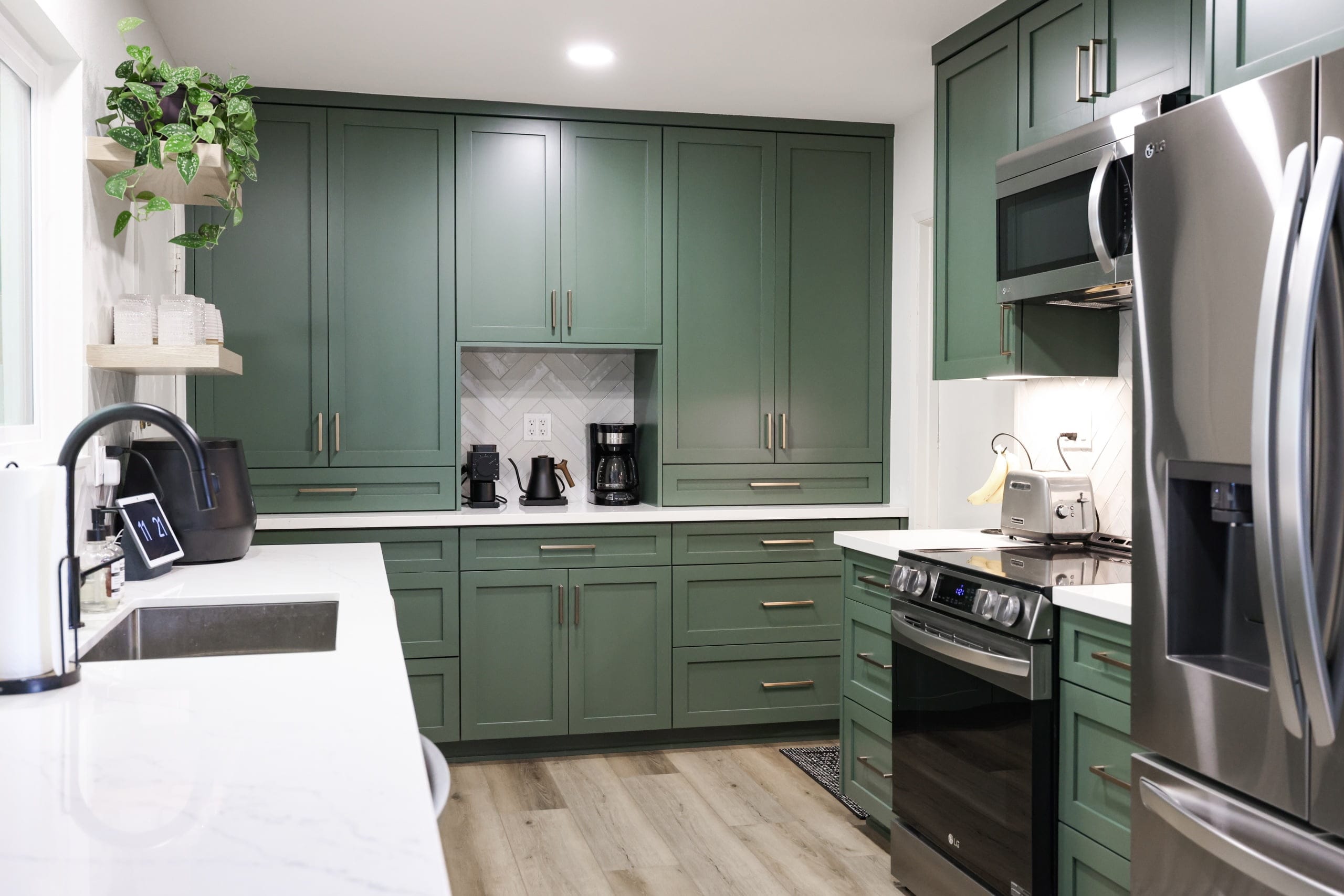 L-shaped green kitchen with quartz counters, stainless appliances and herringbone backsplash