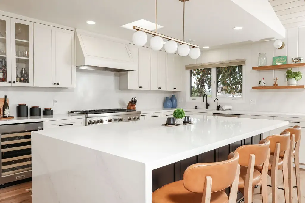 Large white kitchen island with quartz top, pendant lights and leather counter stools