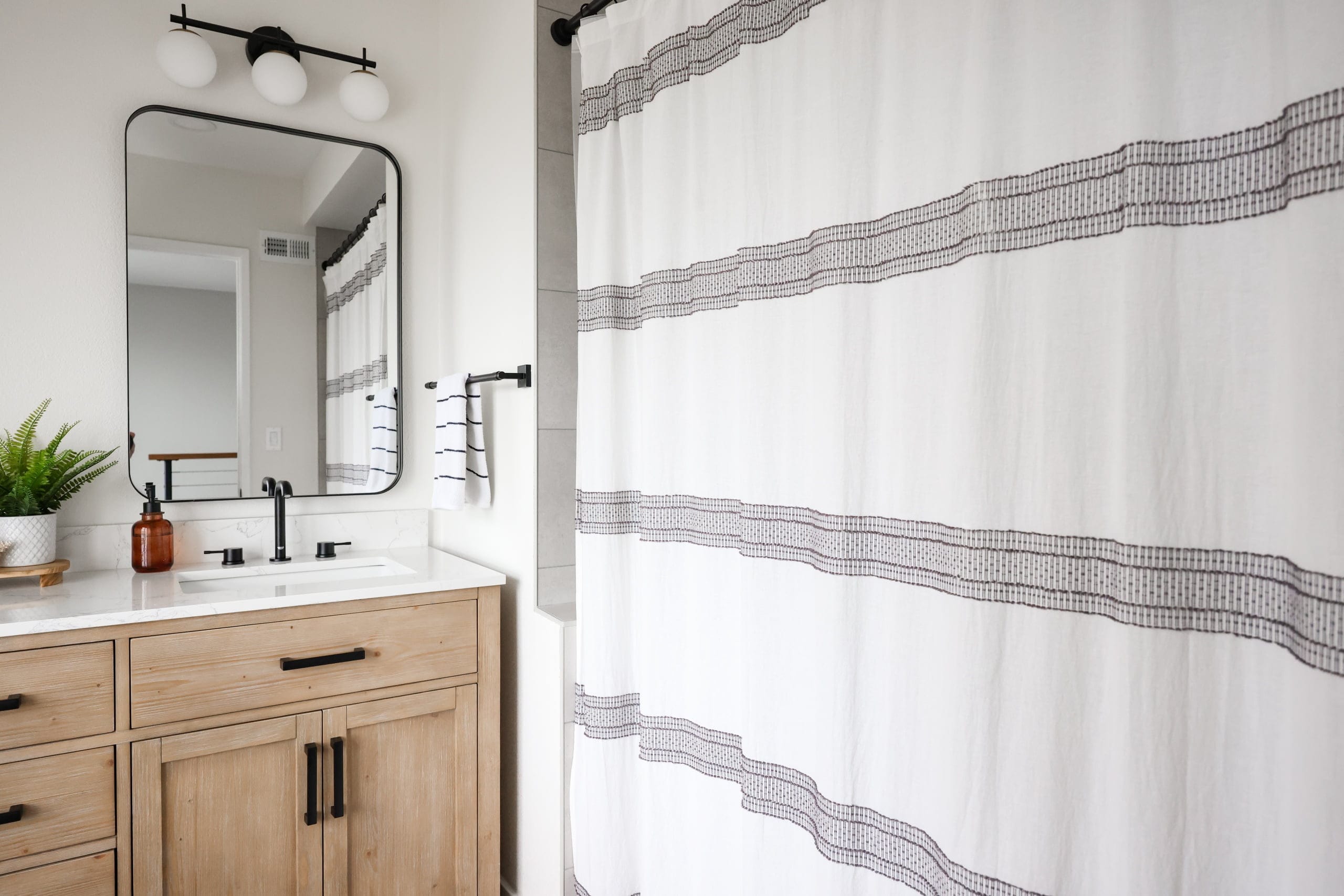Light-oak vanity with marble top beside a gray-striped fabric shower curtain