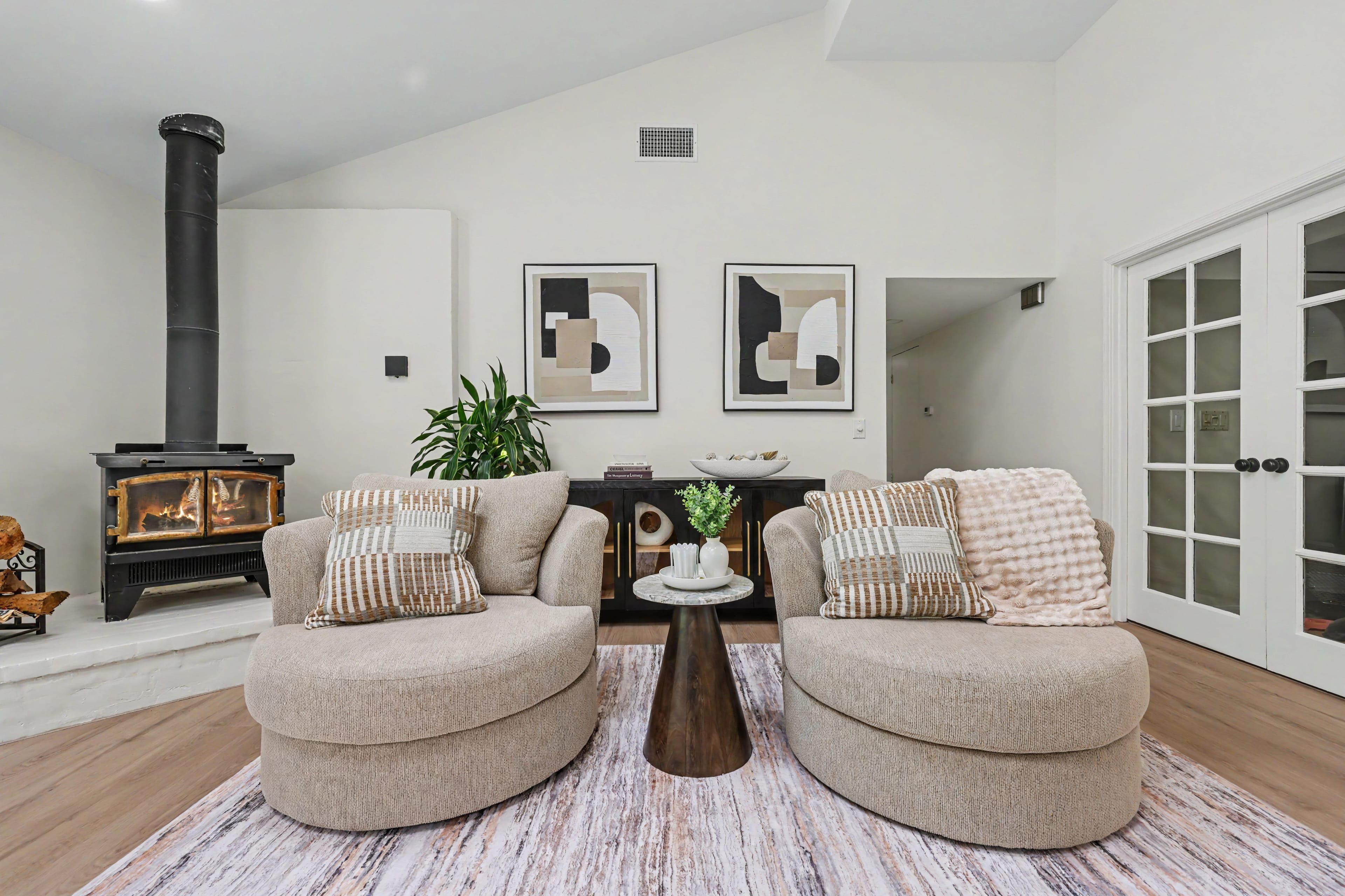 Cozy living room setup with two light tan round swivel chairs, a textured rug, and a freestanding black wood stove on a white hearth.