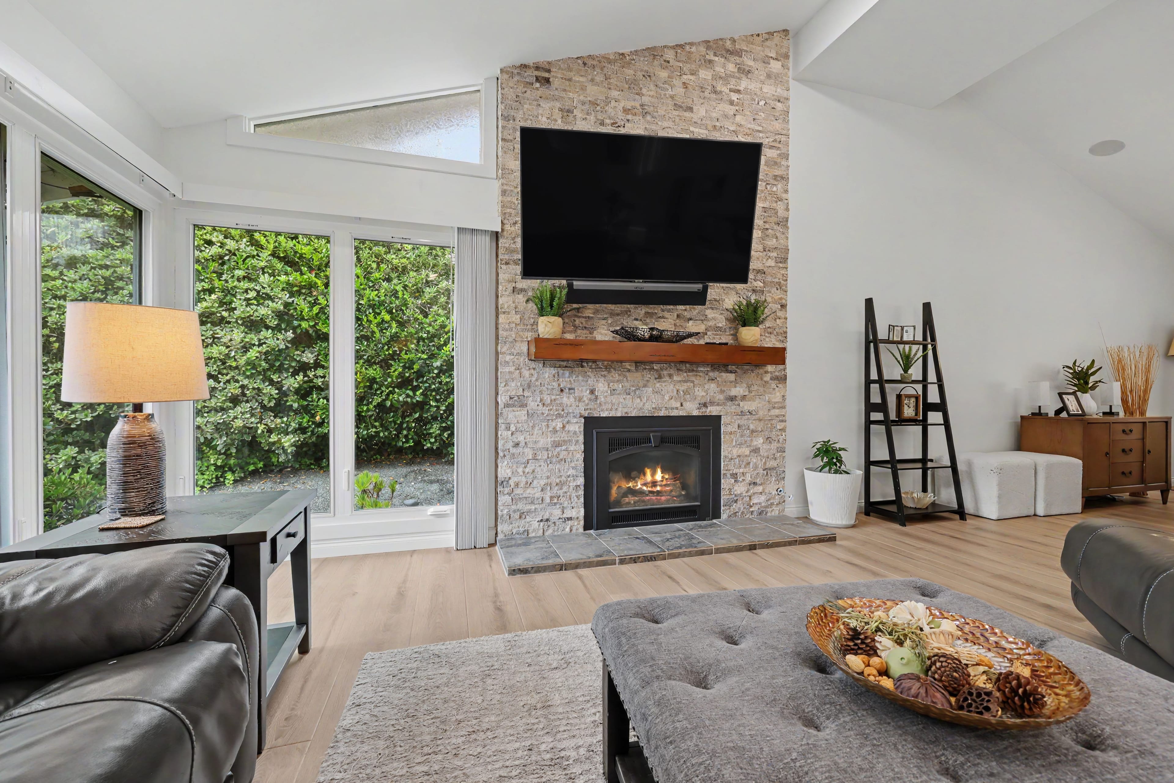 Living room focusing on a floor-to-ceiling textured stone fireplace with a glowing fire, a wooden mantel, and a mounted flat-screen TV.