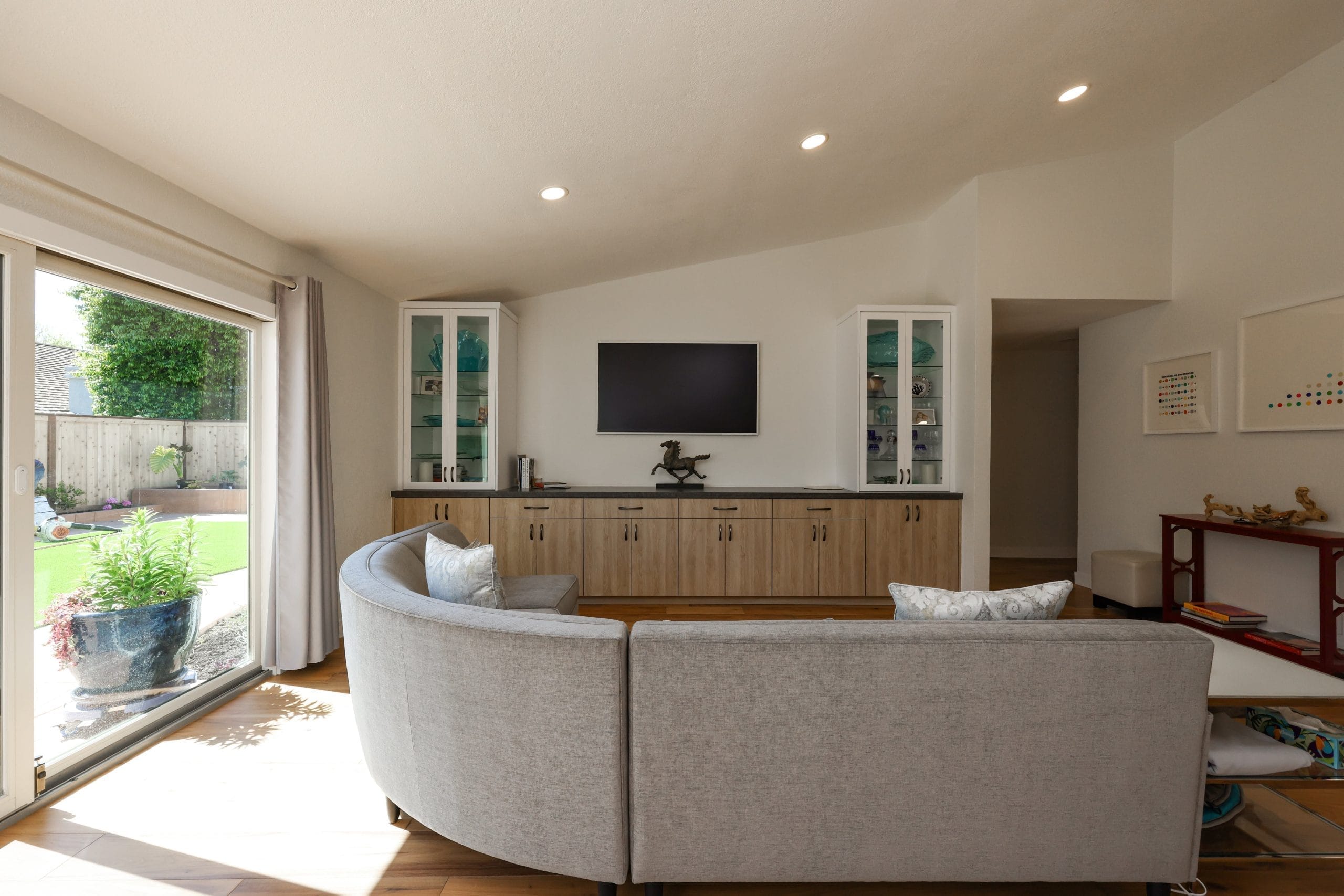 Living room with curved gray sofa, oak media cabinet and patio slider