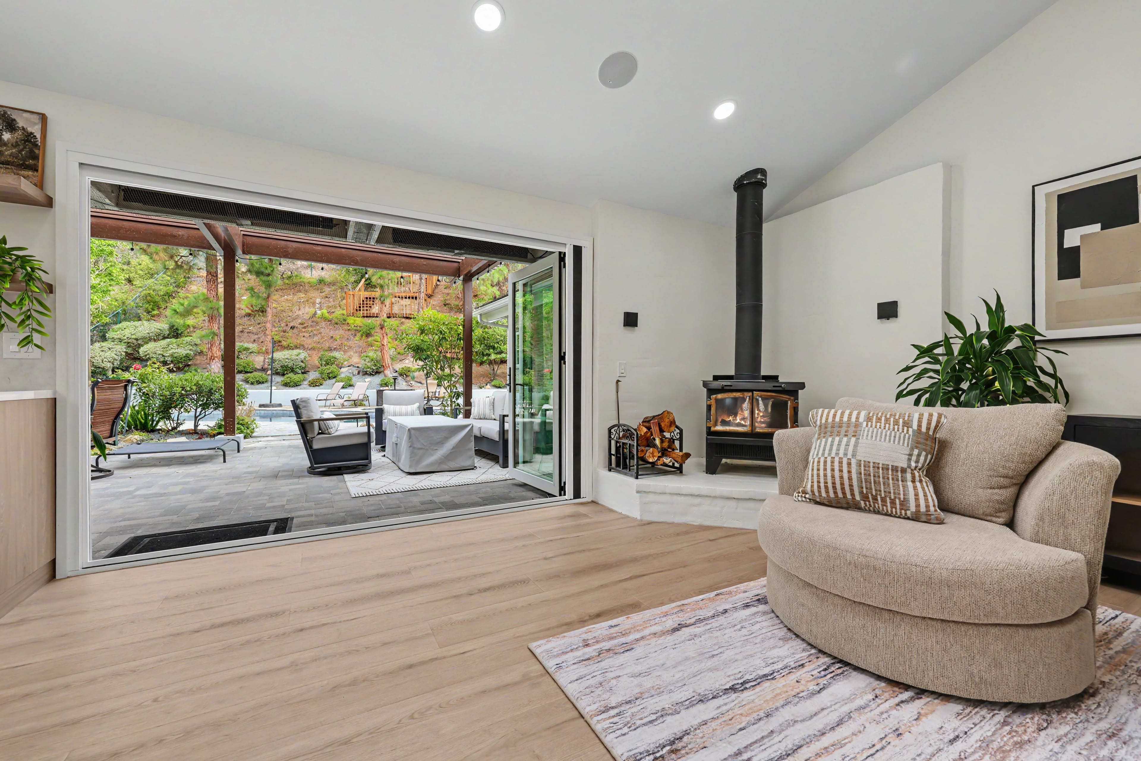 Living area featuring a tan swivel chair and black wood stove next to wide-open accordion glass doors leading to a backyard patio and pergola.