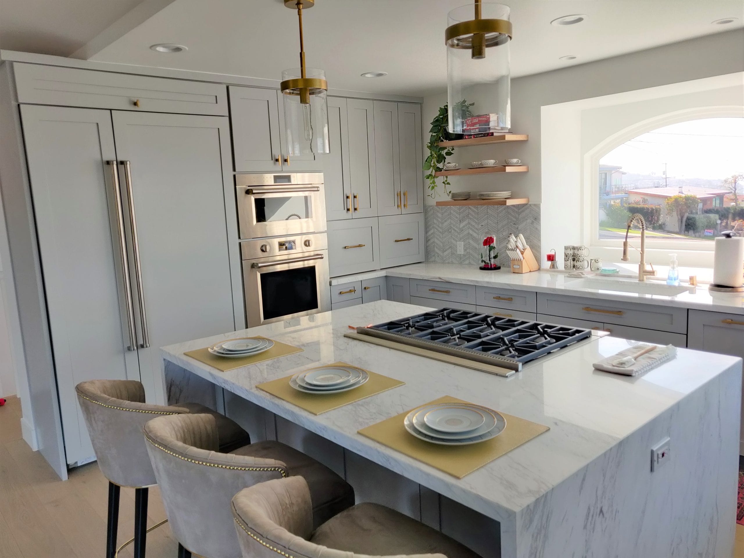 luxury kitchen island with marble top, gas cooktop, and gray nailhead barstools