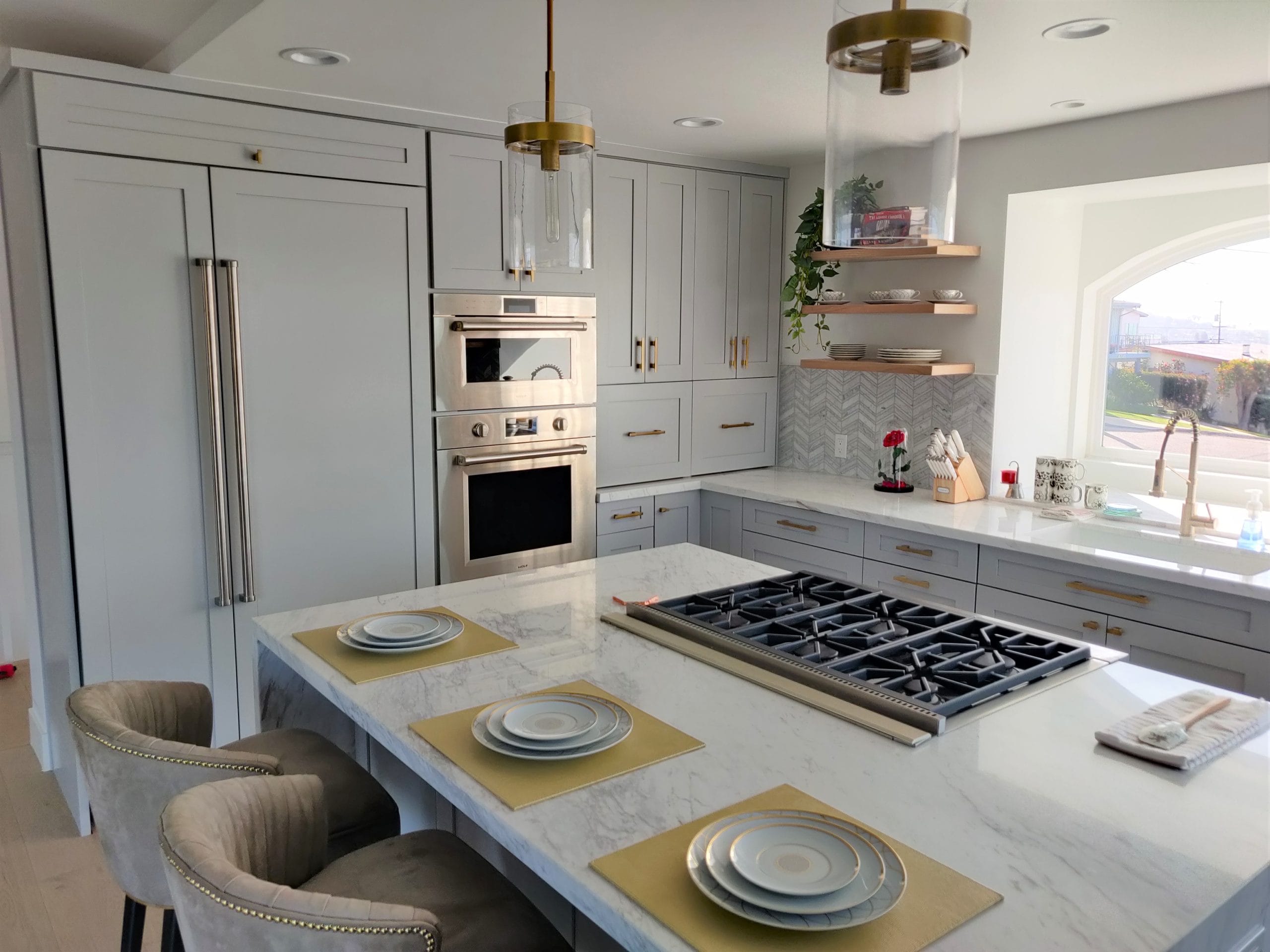 marble island kitchen with pro gas cooktop, gold placemats, and floating wood shelves