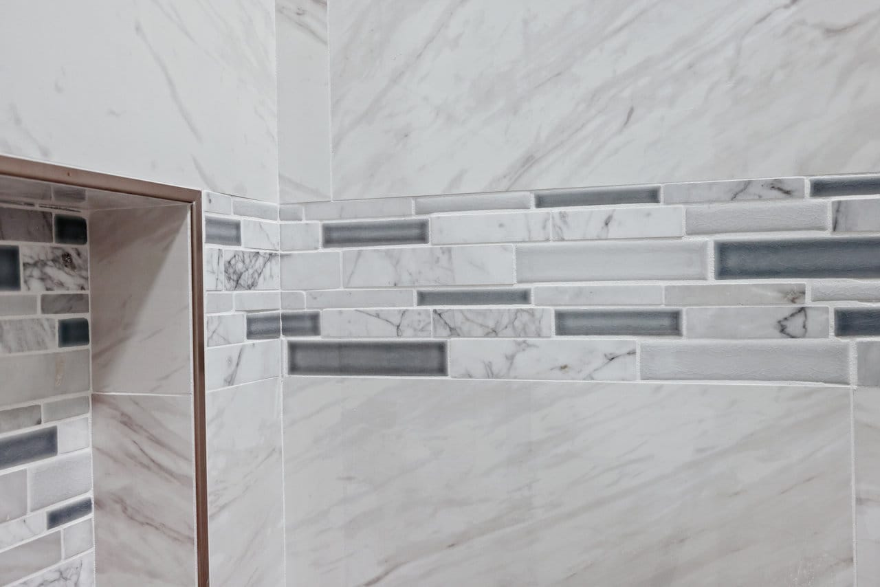 marble-look tile shower wall with horizontal glass mosaic accent band and recessed niche